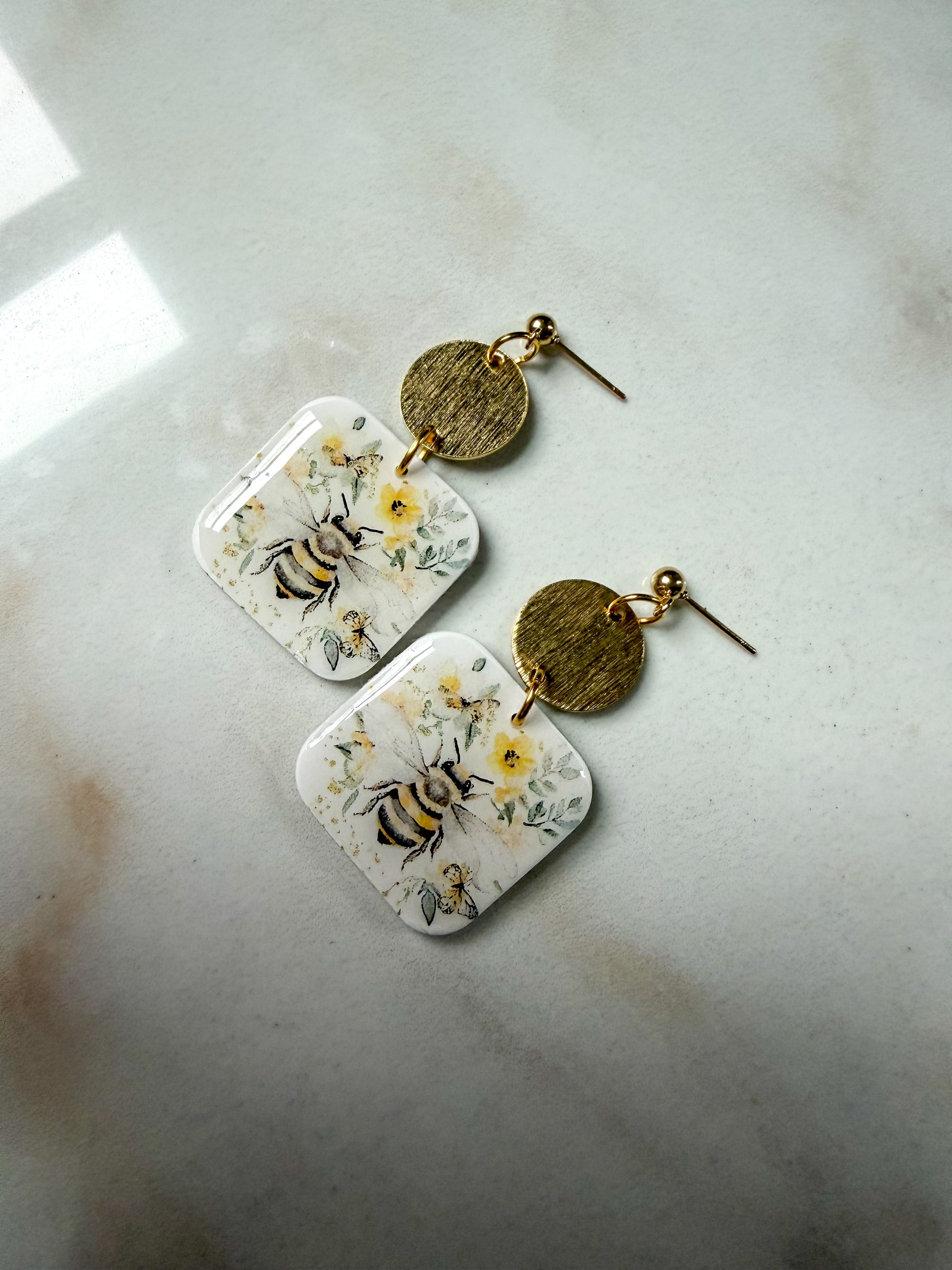 Pair of earrings with floral and bee design on a light surface