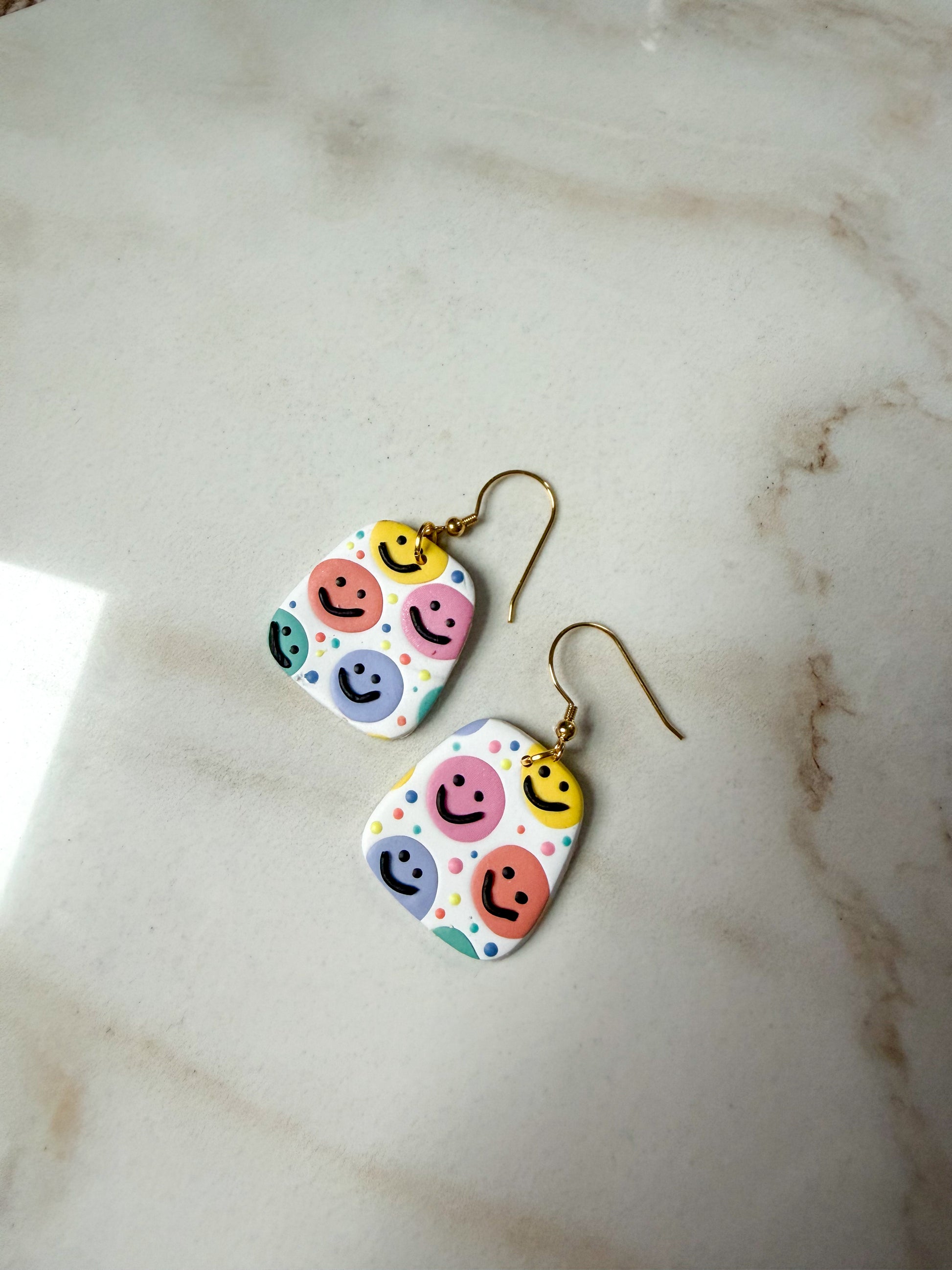 Earrings with a colorful smiley face design laying on a marble surface