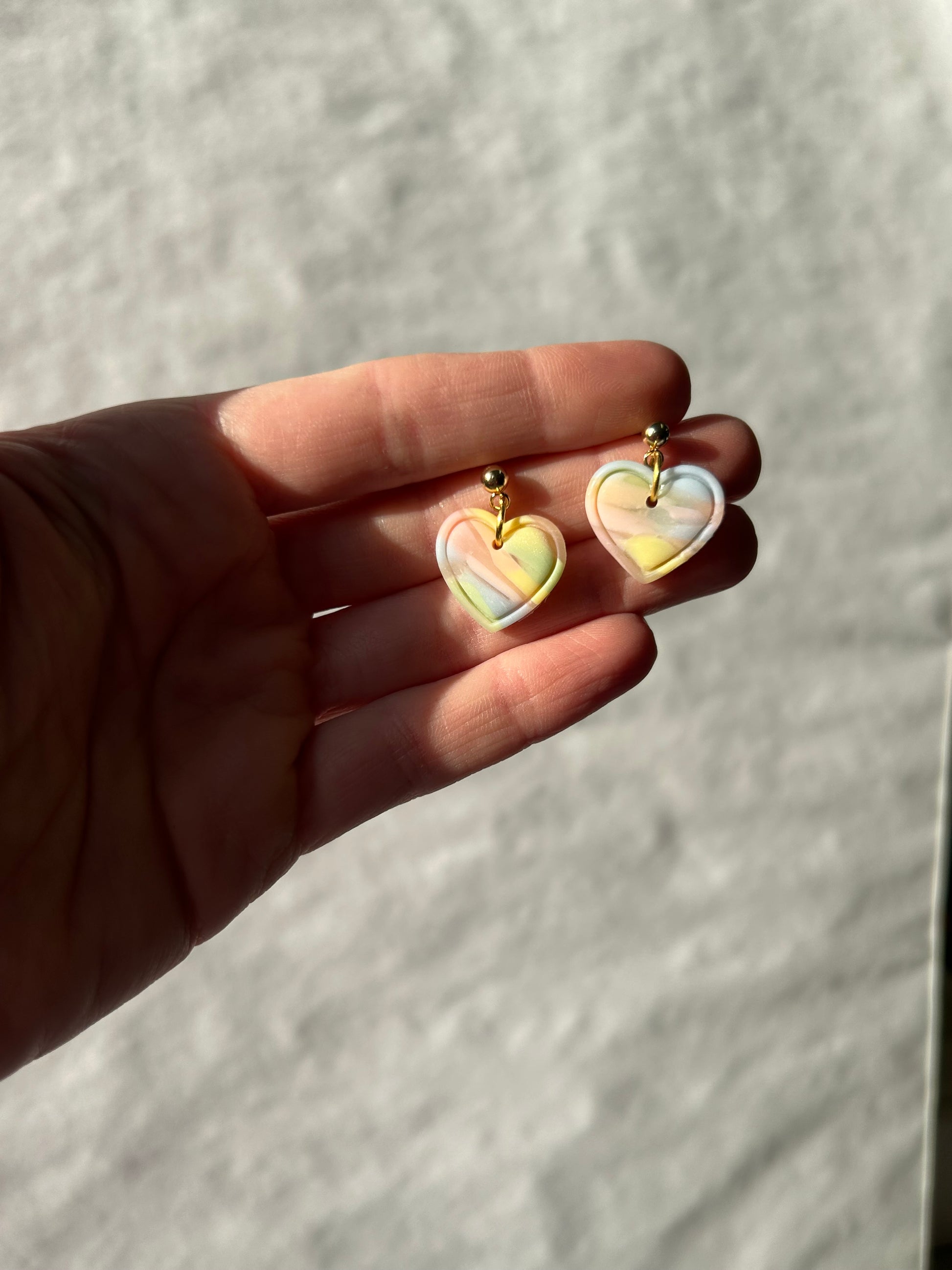 Two heart-shaped earrings held in a hand against a neutral background