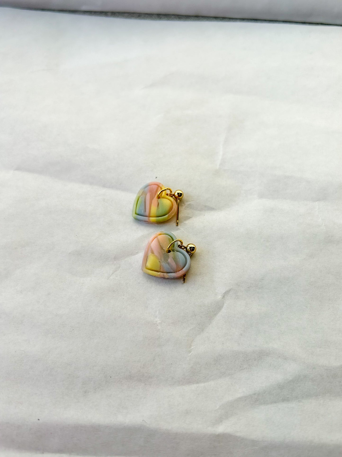 Heart-shaped earrings with rainbow design on a white fabric background