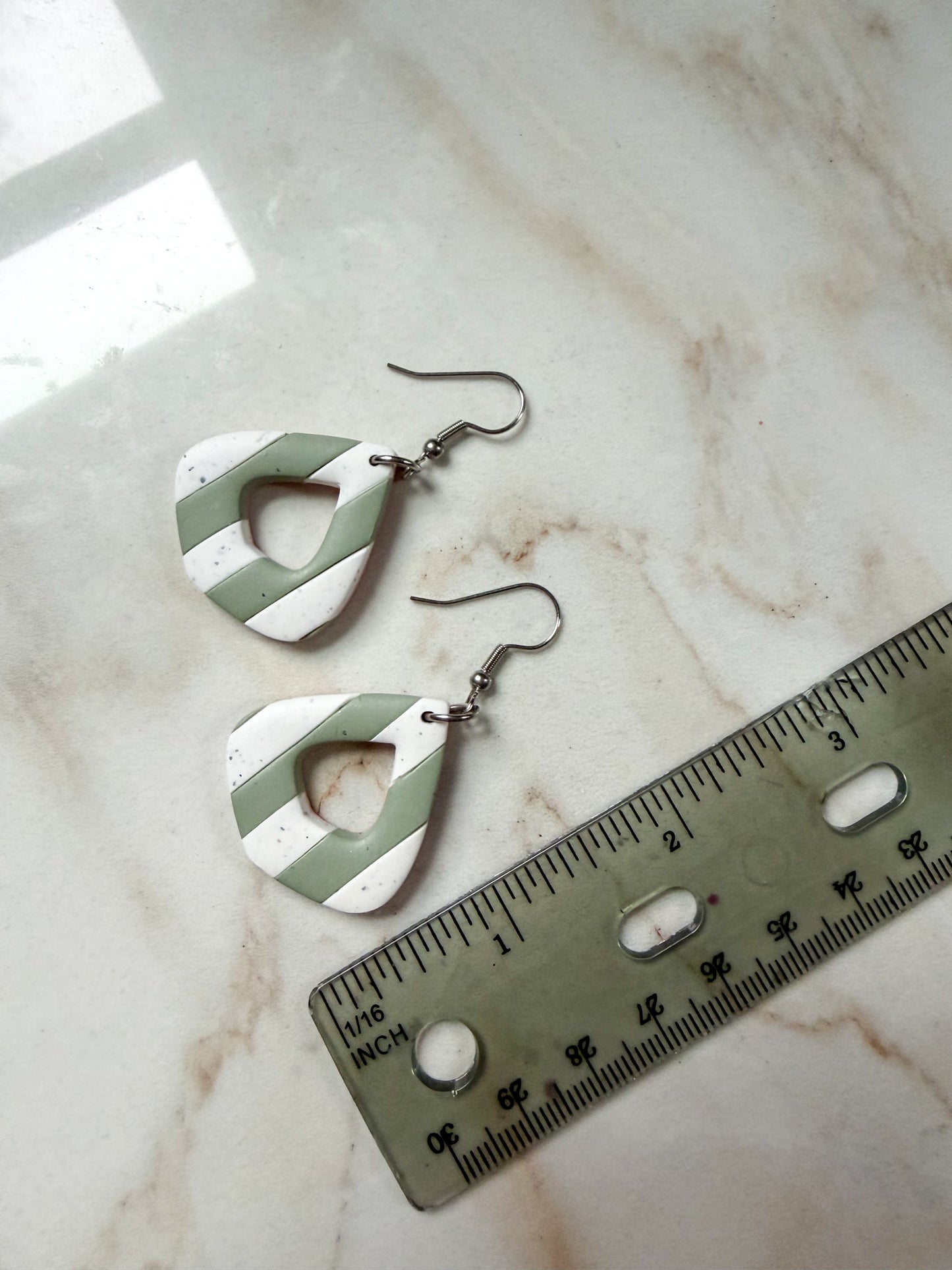 Green and white earrings on a marble surface with a ruler for scale. About 2 inches long. 