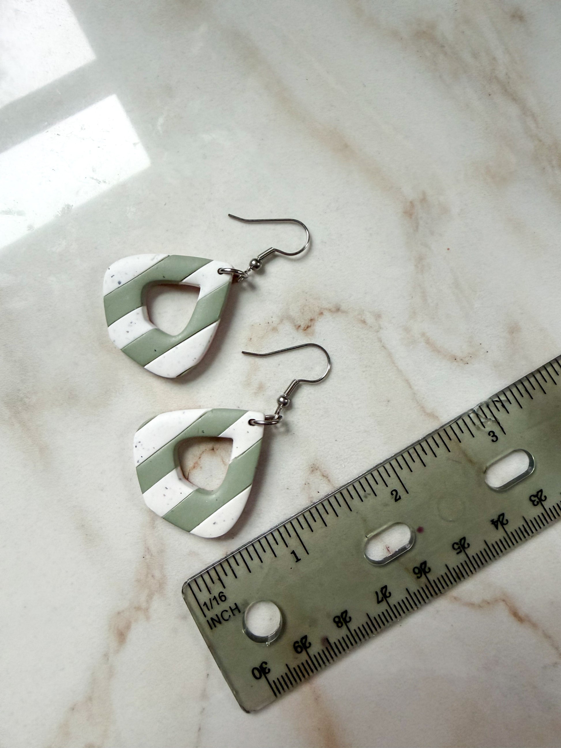 Green and white earrings on a marble surface with a ruler for scale. About 2 inches long. 