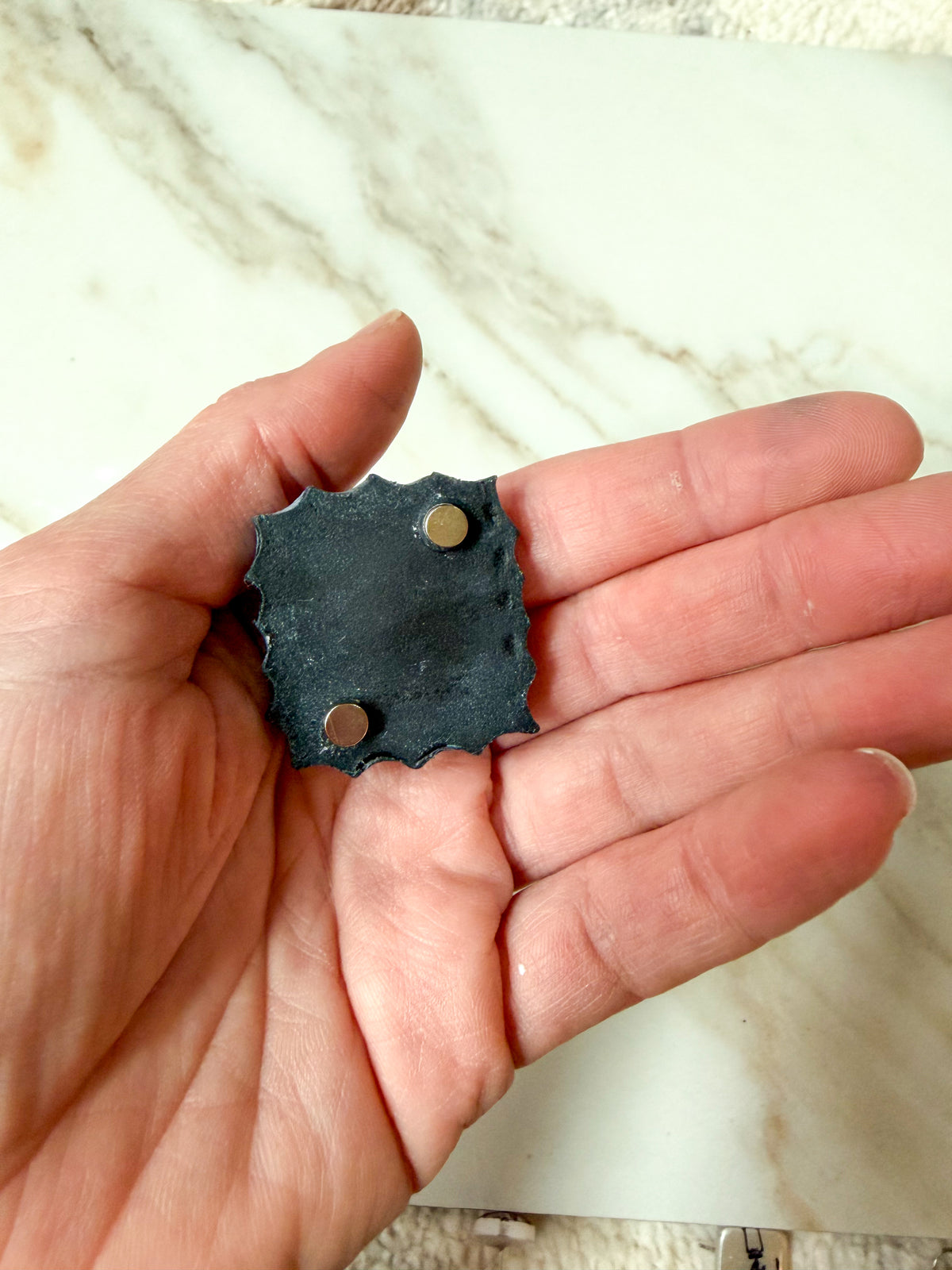 A hand holding a magnet against a marble surface. 