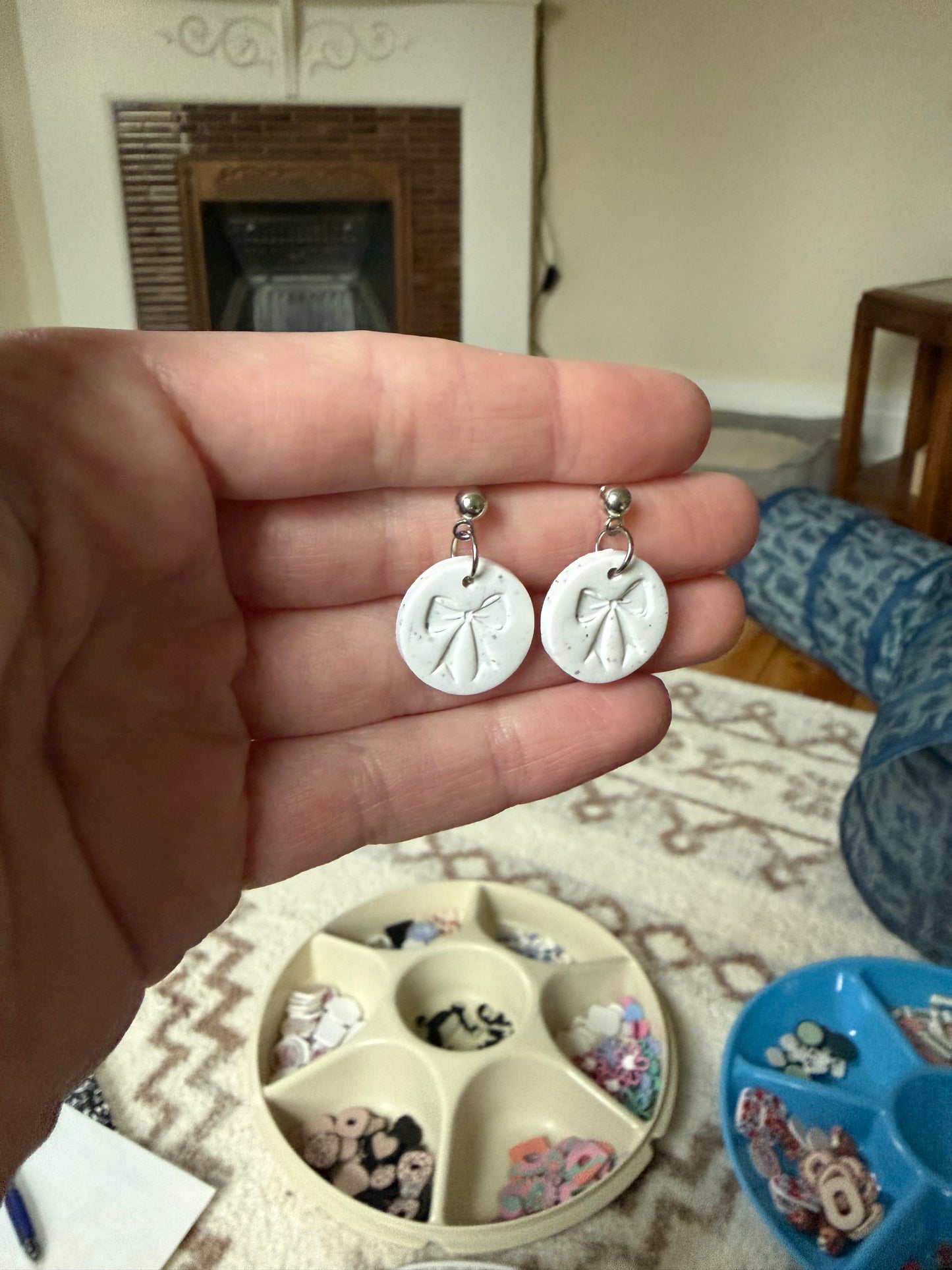 Hand holding a pair of white earrings with a bow shaped stamp.