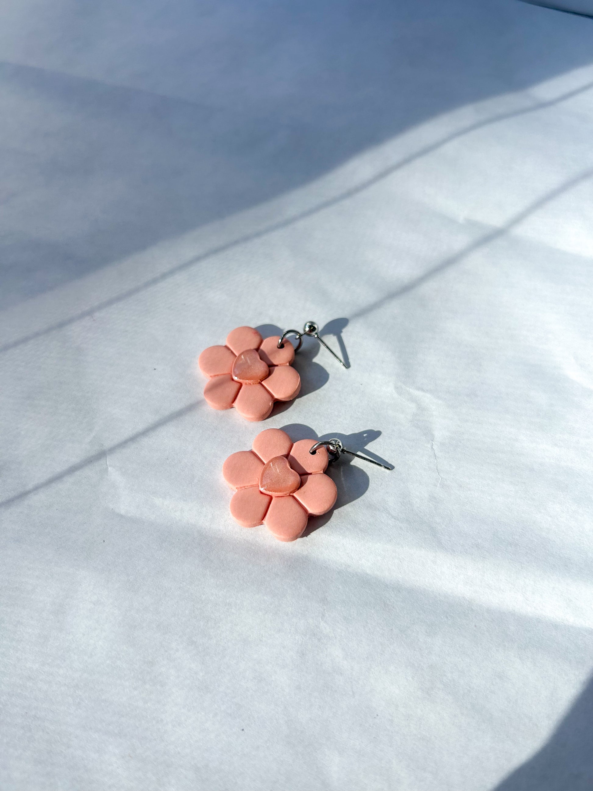 Pink flower-shaped earrings on a white fabric background