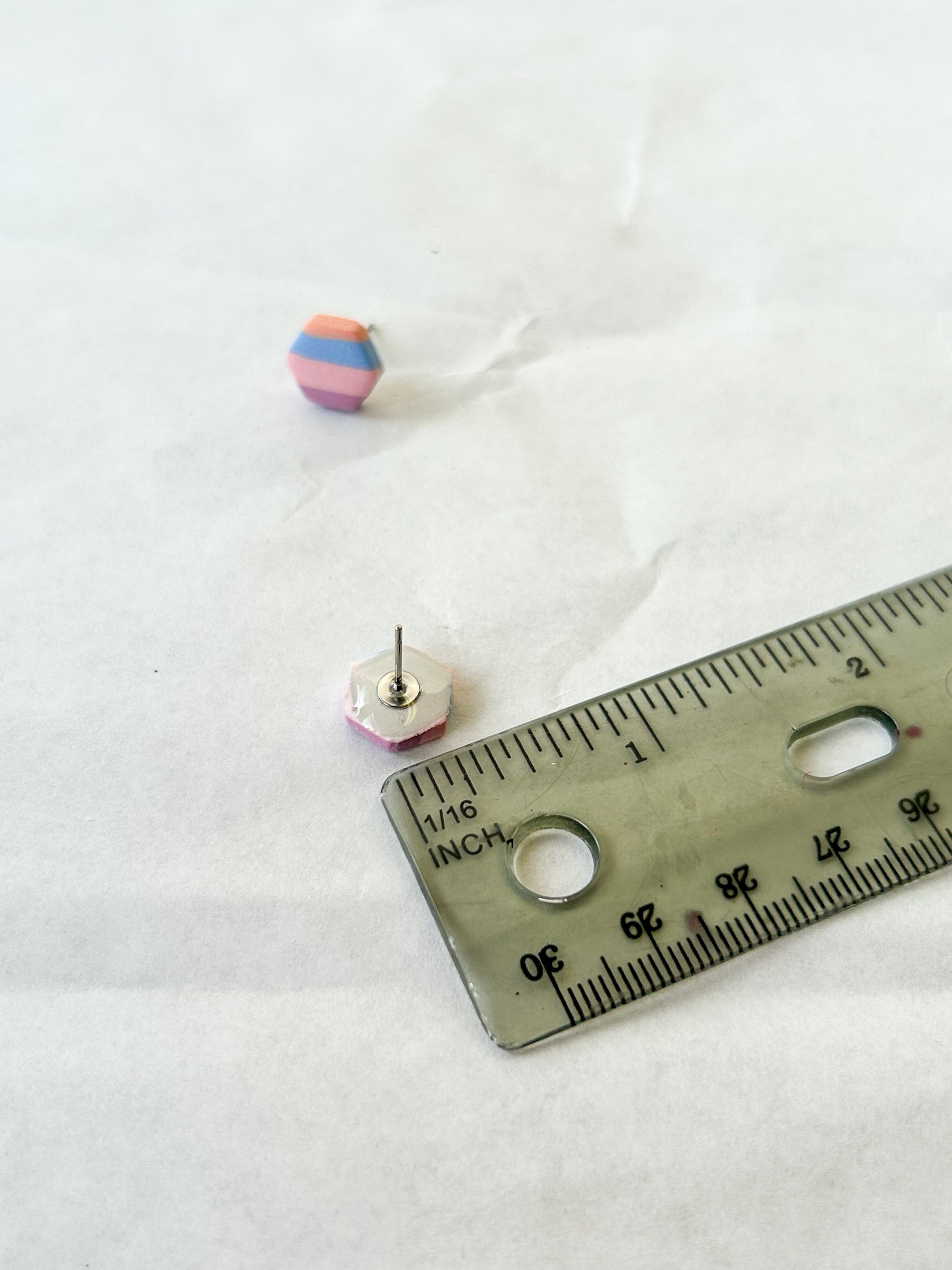 Small colorful earrings next to a ruler on a white background
A little less than a half inch in length
