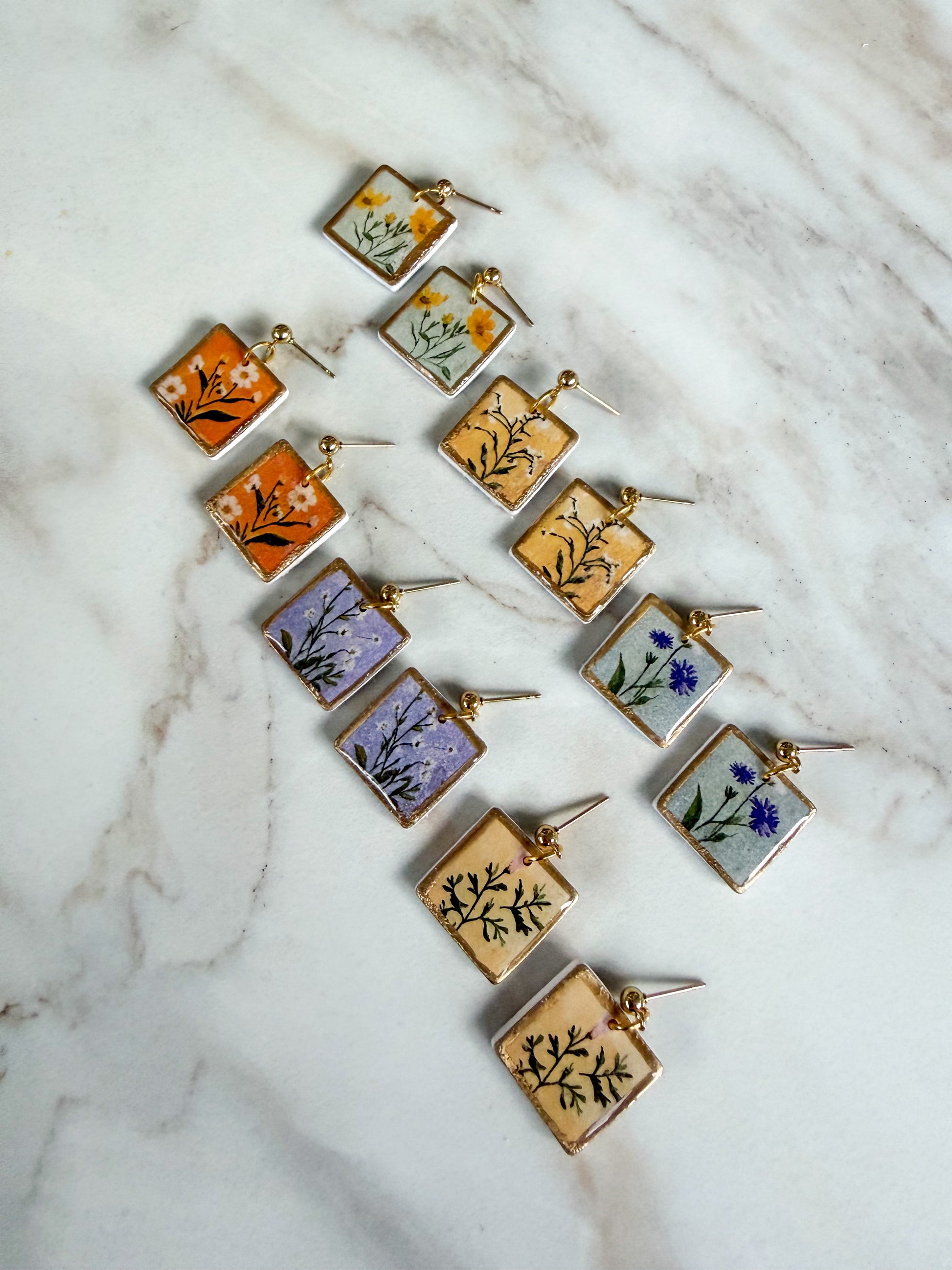 Set of square earrings with floral designs on a marble surface
