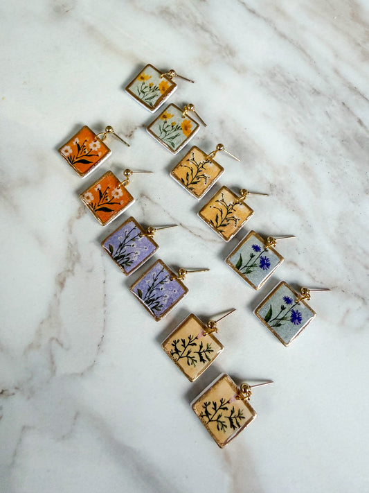 Set of square earrings with floral designs on a marble surface