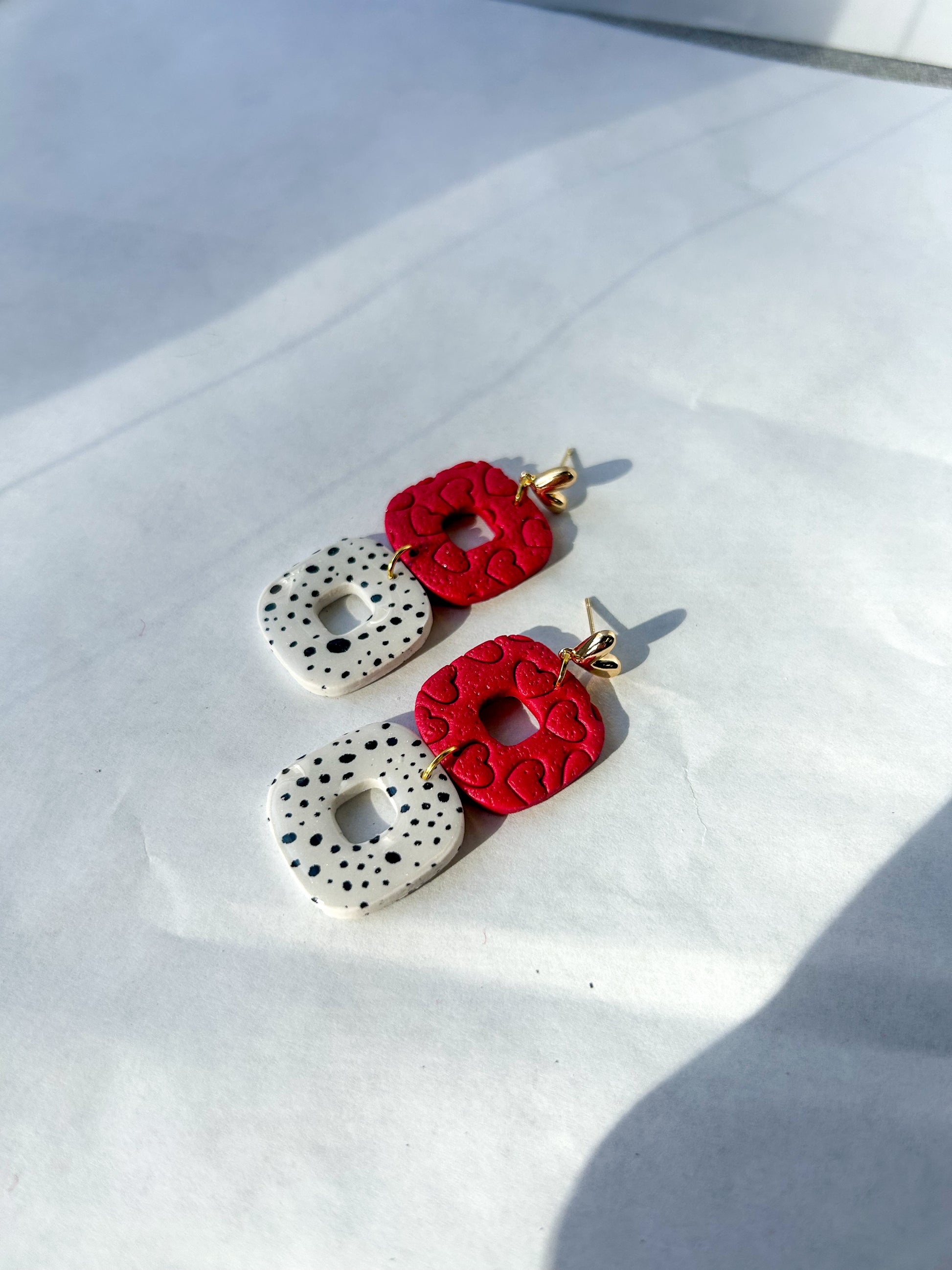 Pair of earrings with red floral and white textured designs on a white surface.
