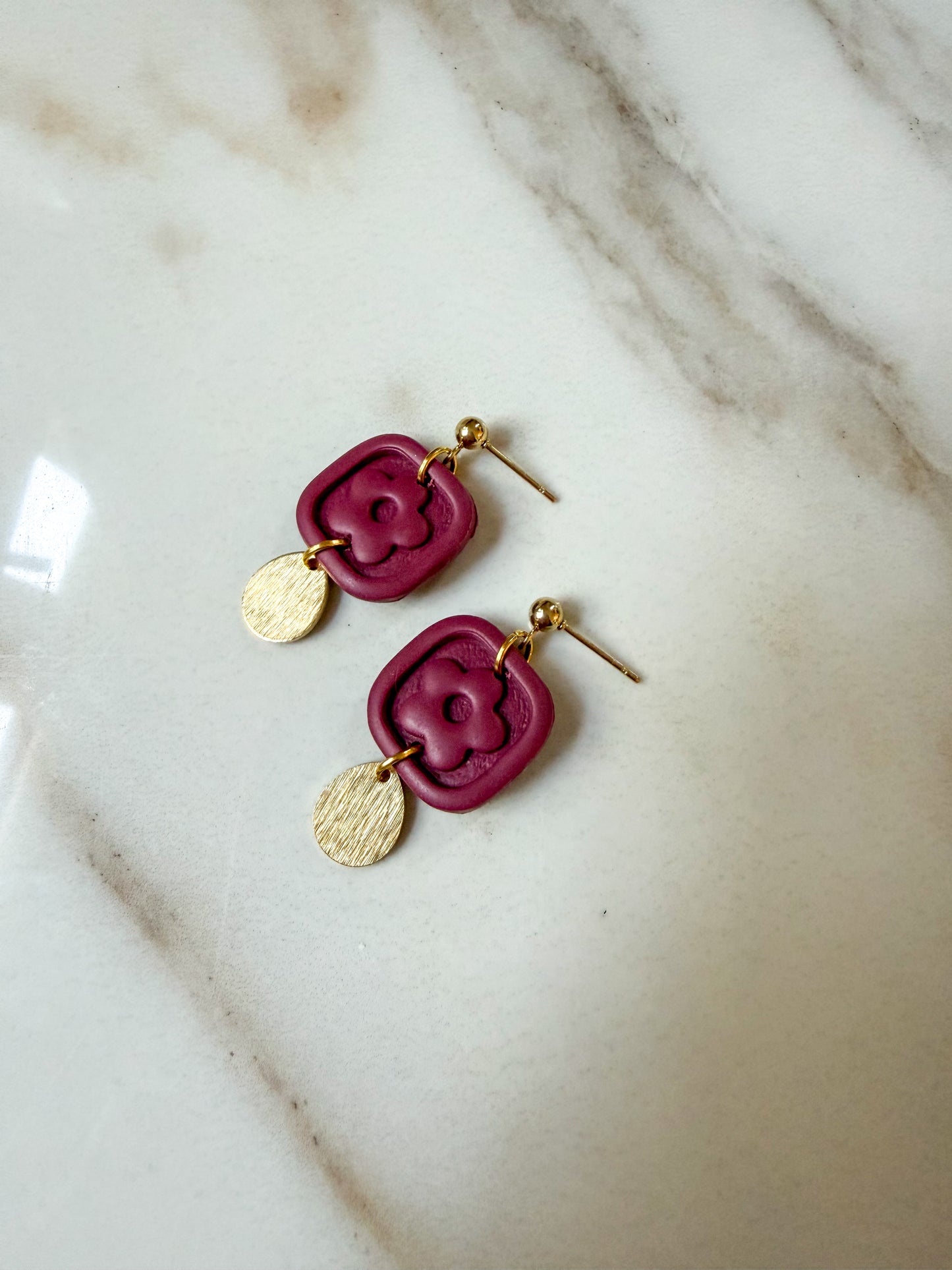 Burgundy flower dangles with a brass charm laying on a marble surface. 