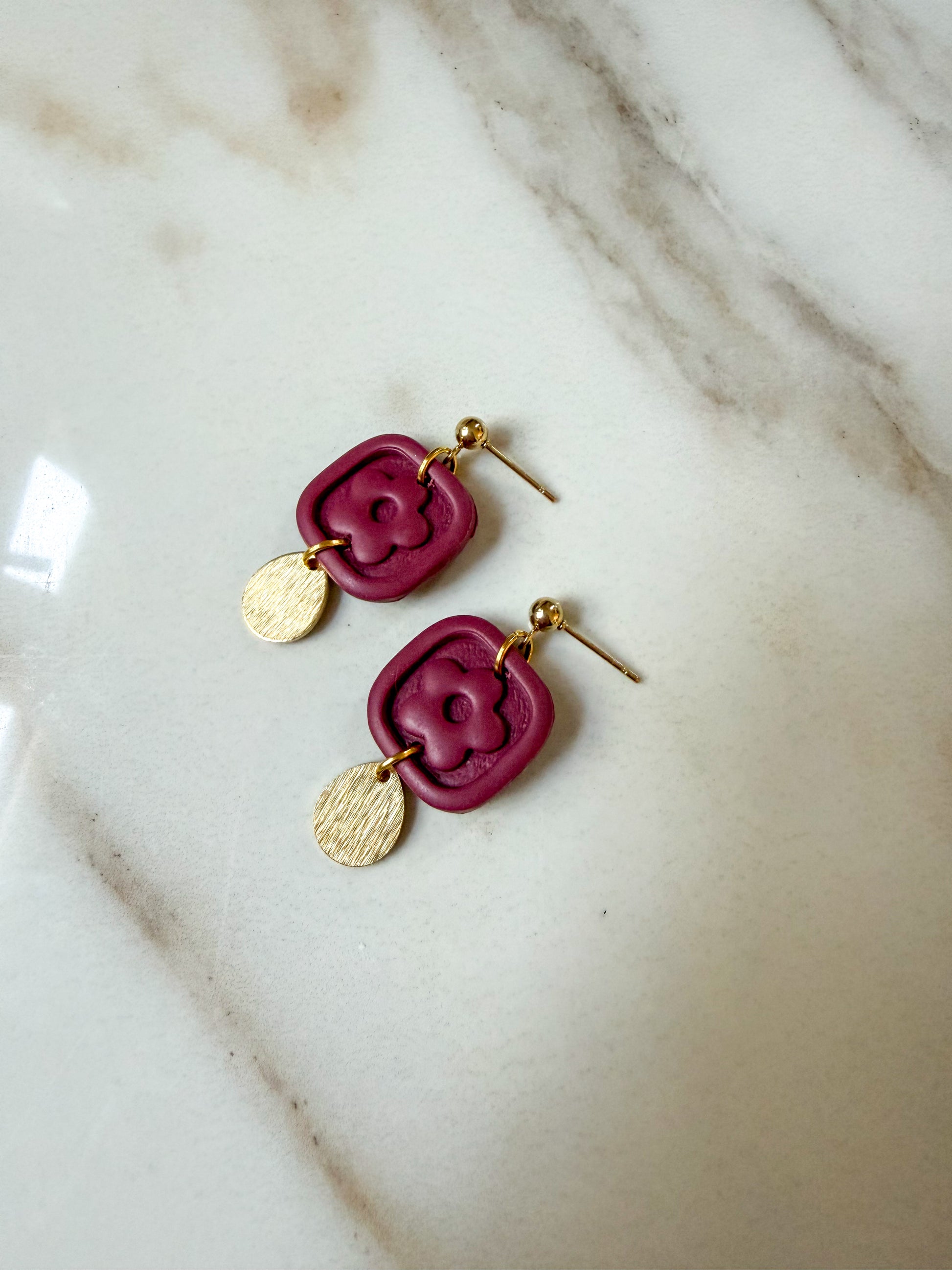 Burgundy flower dangles with a brass charm laying on a marble surface. 