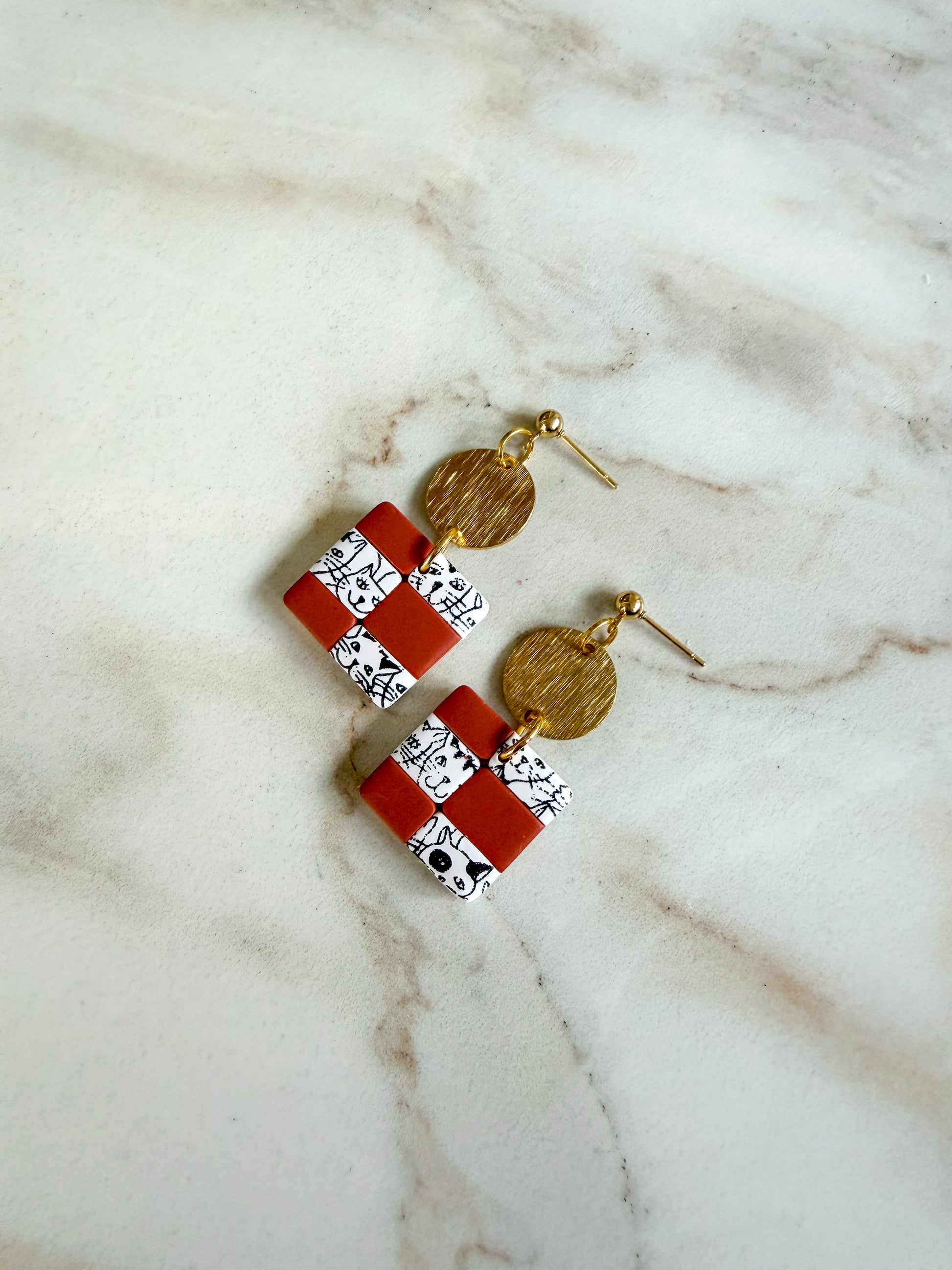Pair of earrings with red and white square designs on a marble surface