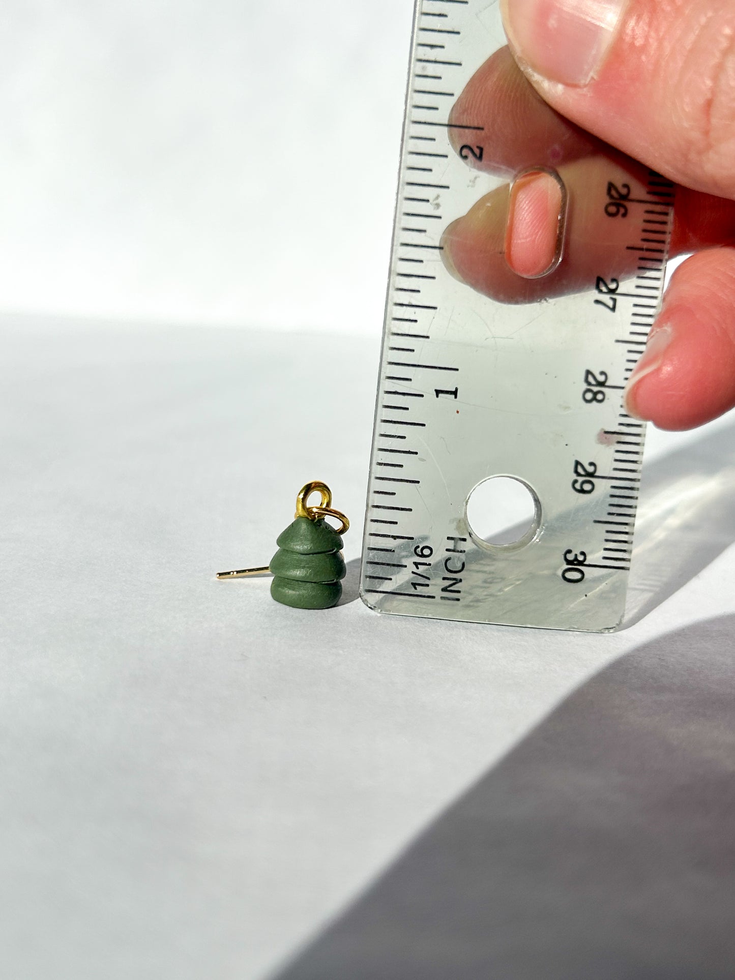 Green Christmas tree-shaped earring being measured with a ruler on a white background. About half an inch in height