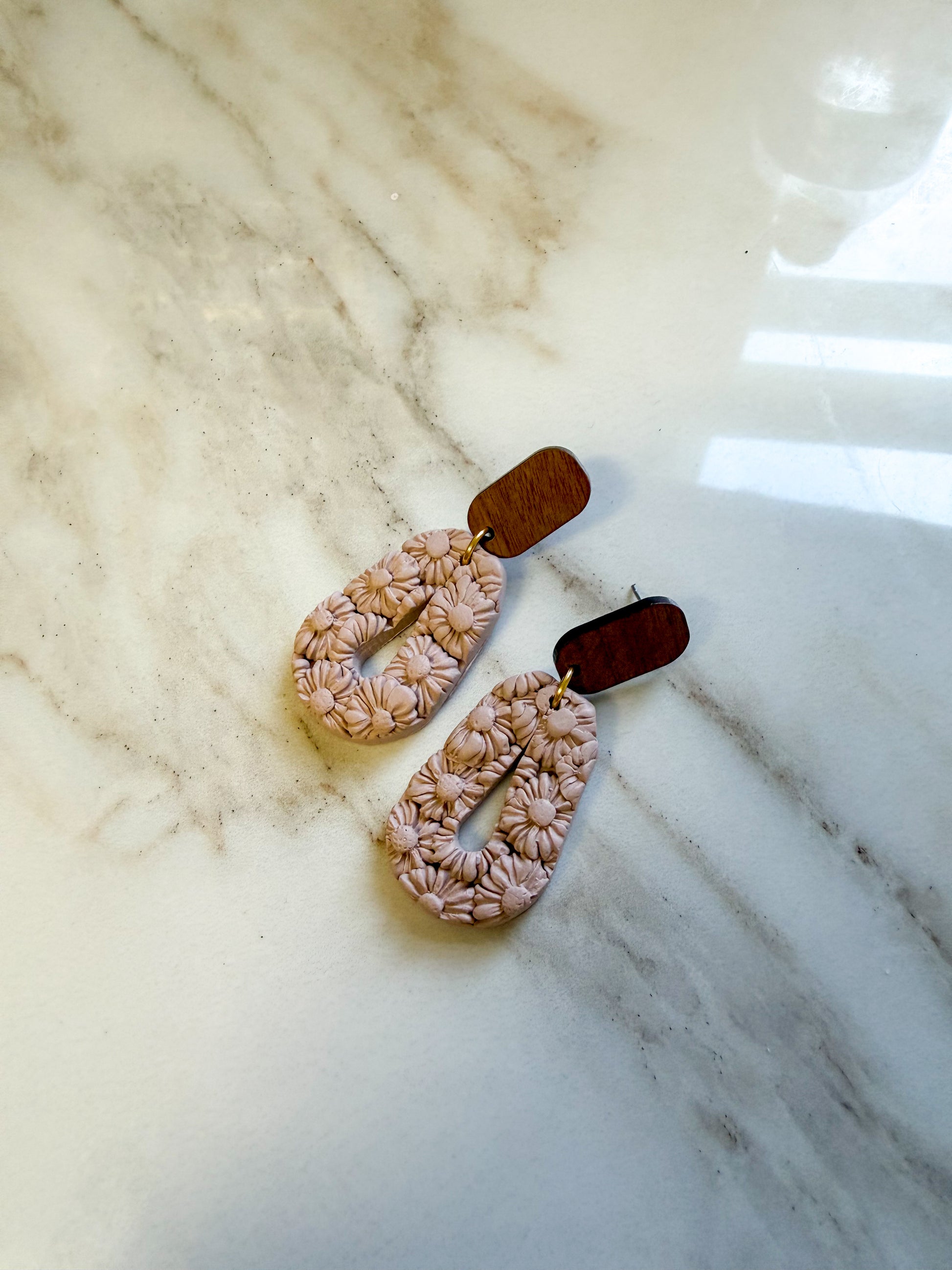 Floral earrings on a marble surface. The earrings have textured flowers covering the surface. 