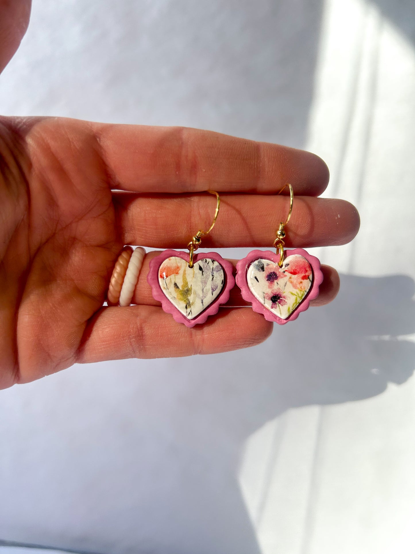 Heart-shaped earrings with floral design held in a hand against a white background