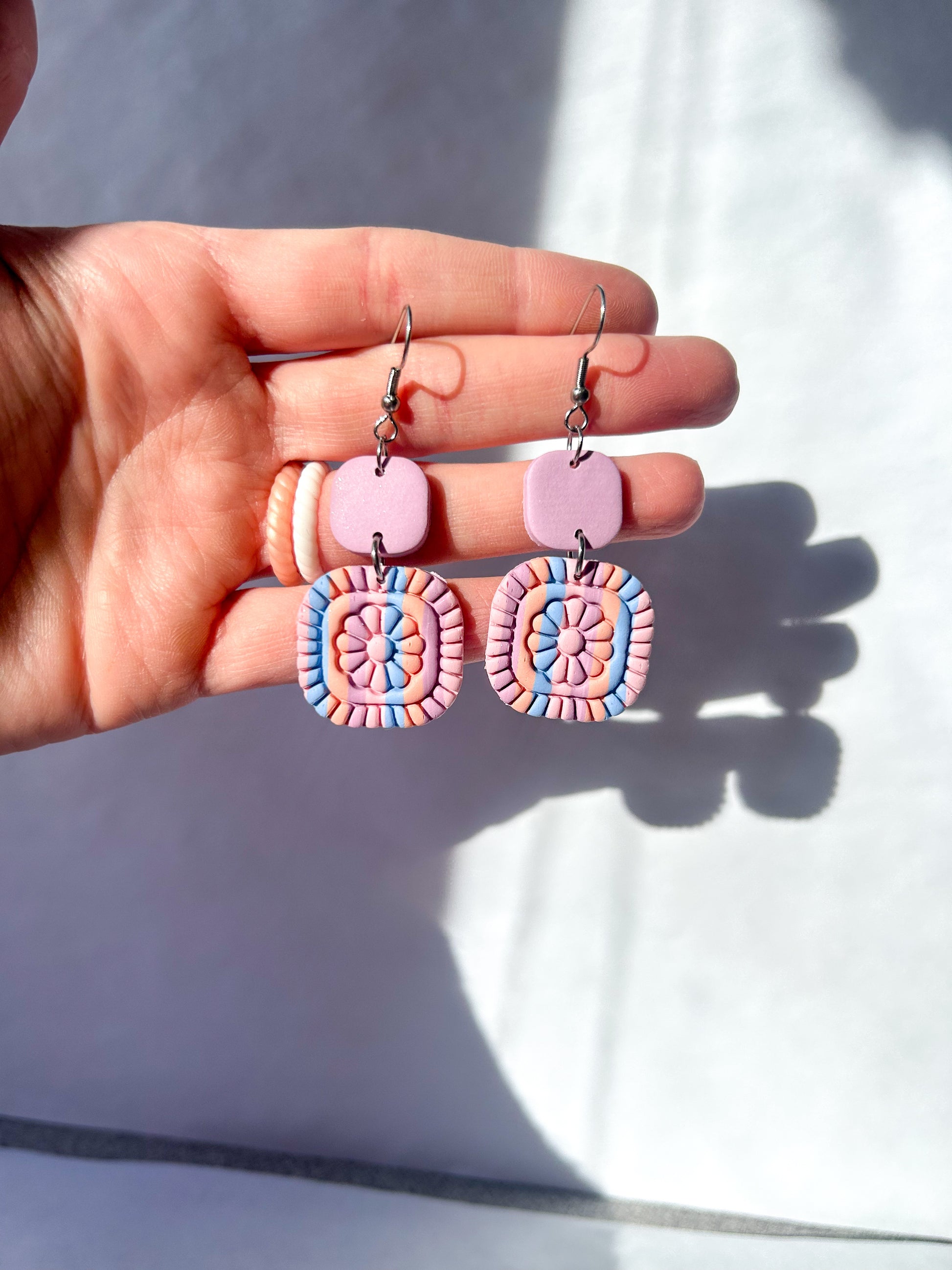 Hand holding a pair of colorful earrings with a light background