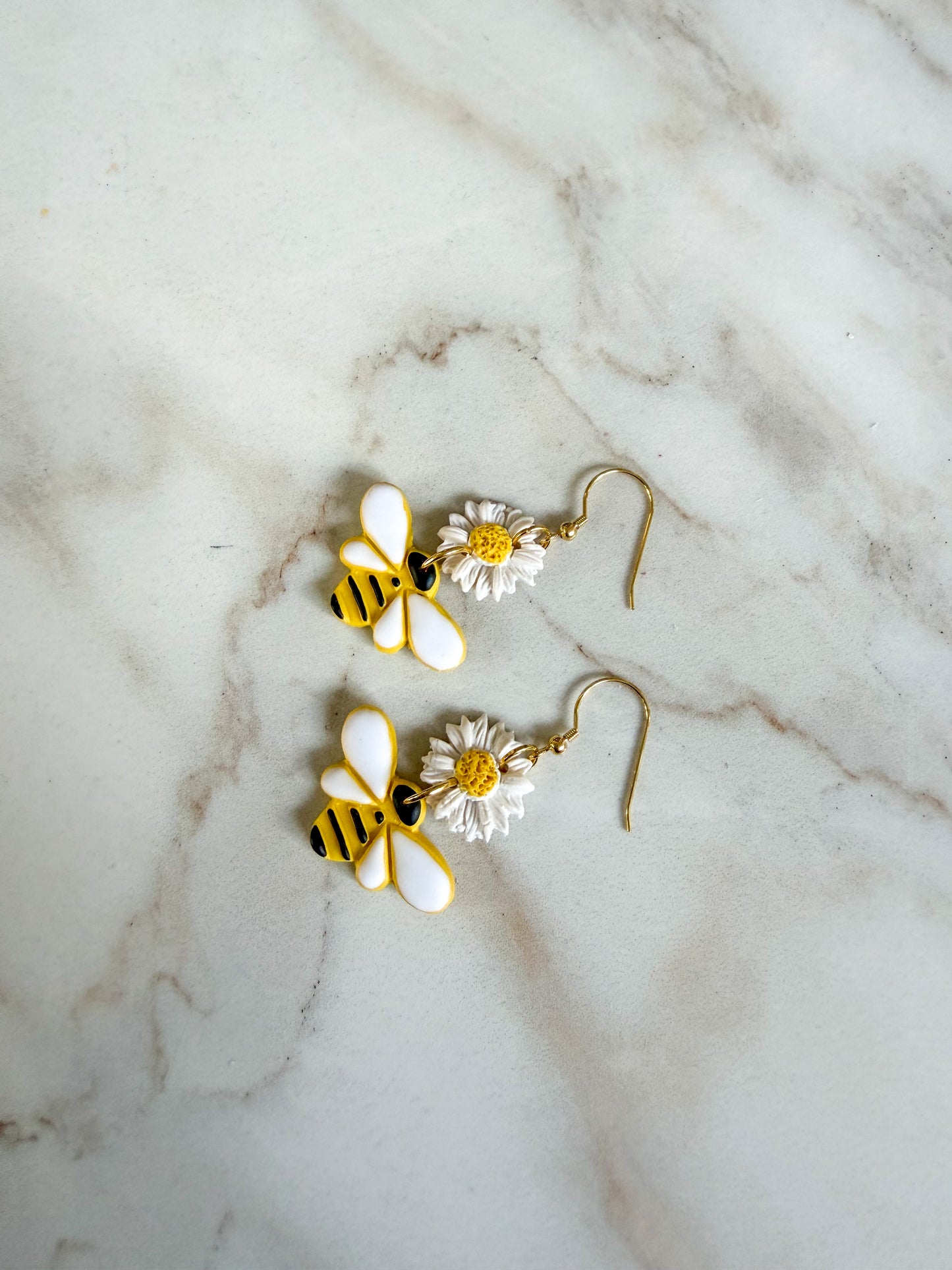 Bee-shaped earrings with white and yellow details on a marble surface