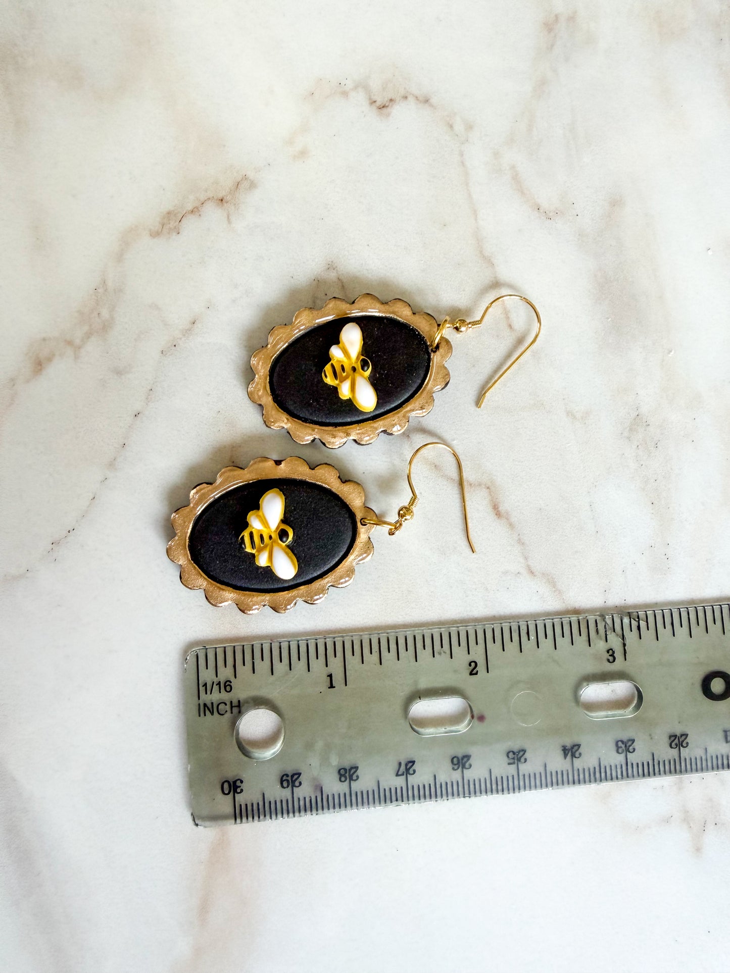 Pair of earrings with black and gold design on a marble surface with a ruler for scale. About 2 inches long 