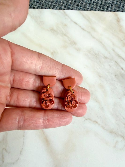 Hand holding a pair of orange flower-shaped earrings on a white marble surface.