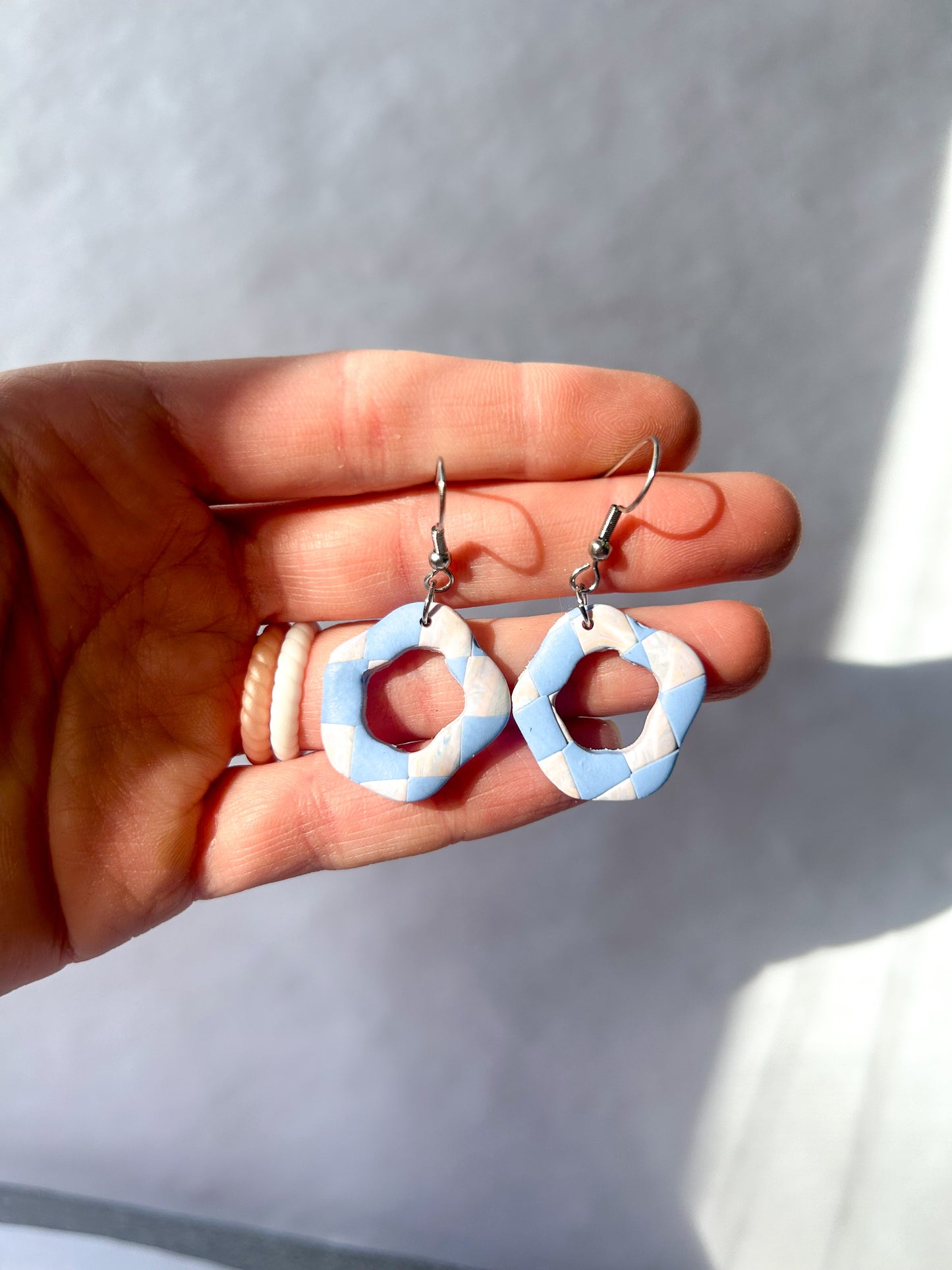 Hand holding a pair of checker pattern earrings with a cut out in the center