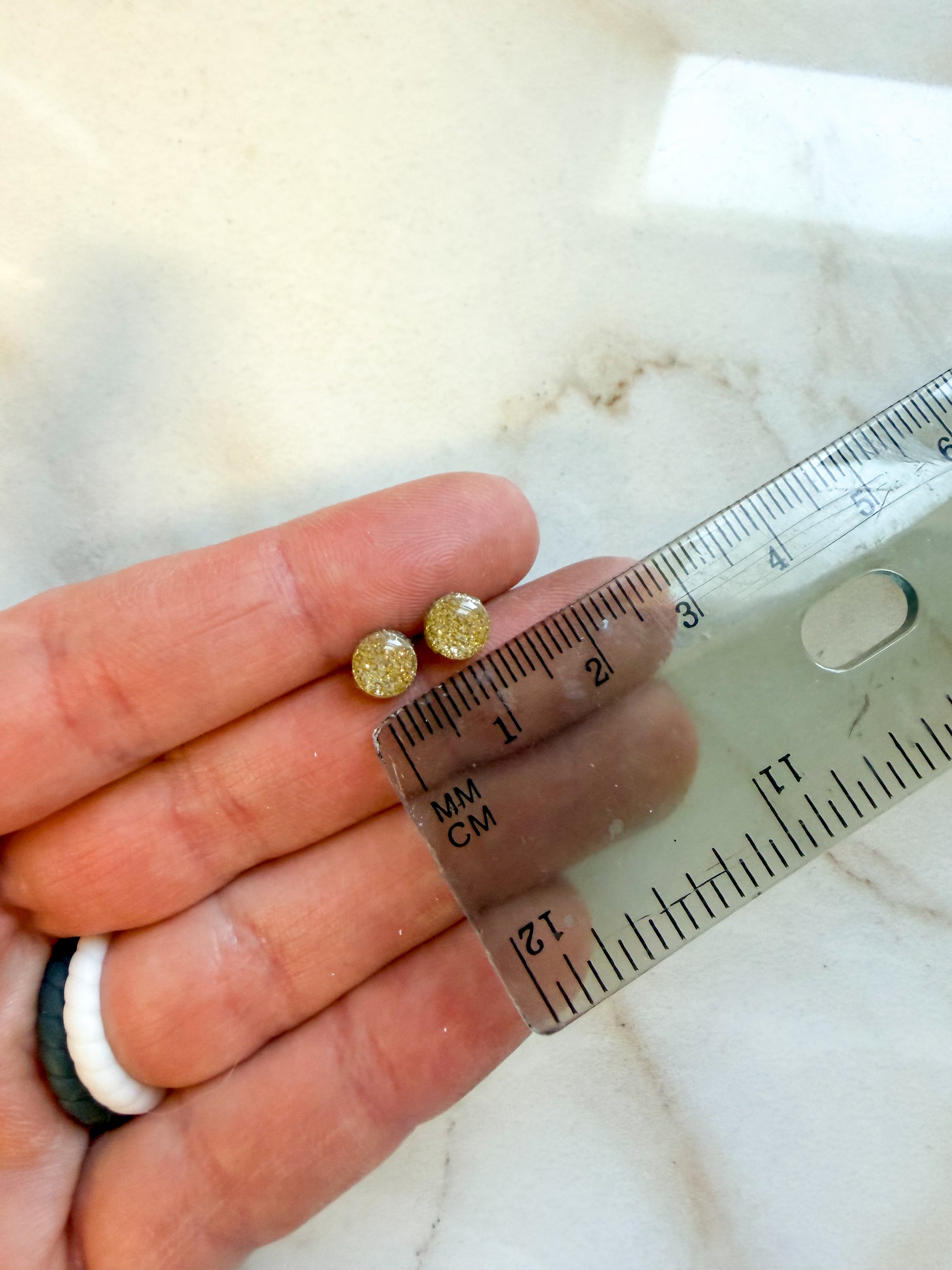 Two small golden earring studs held against a ruler for scale. Each earring is about 1/2 centimeter in width. 