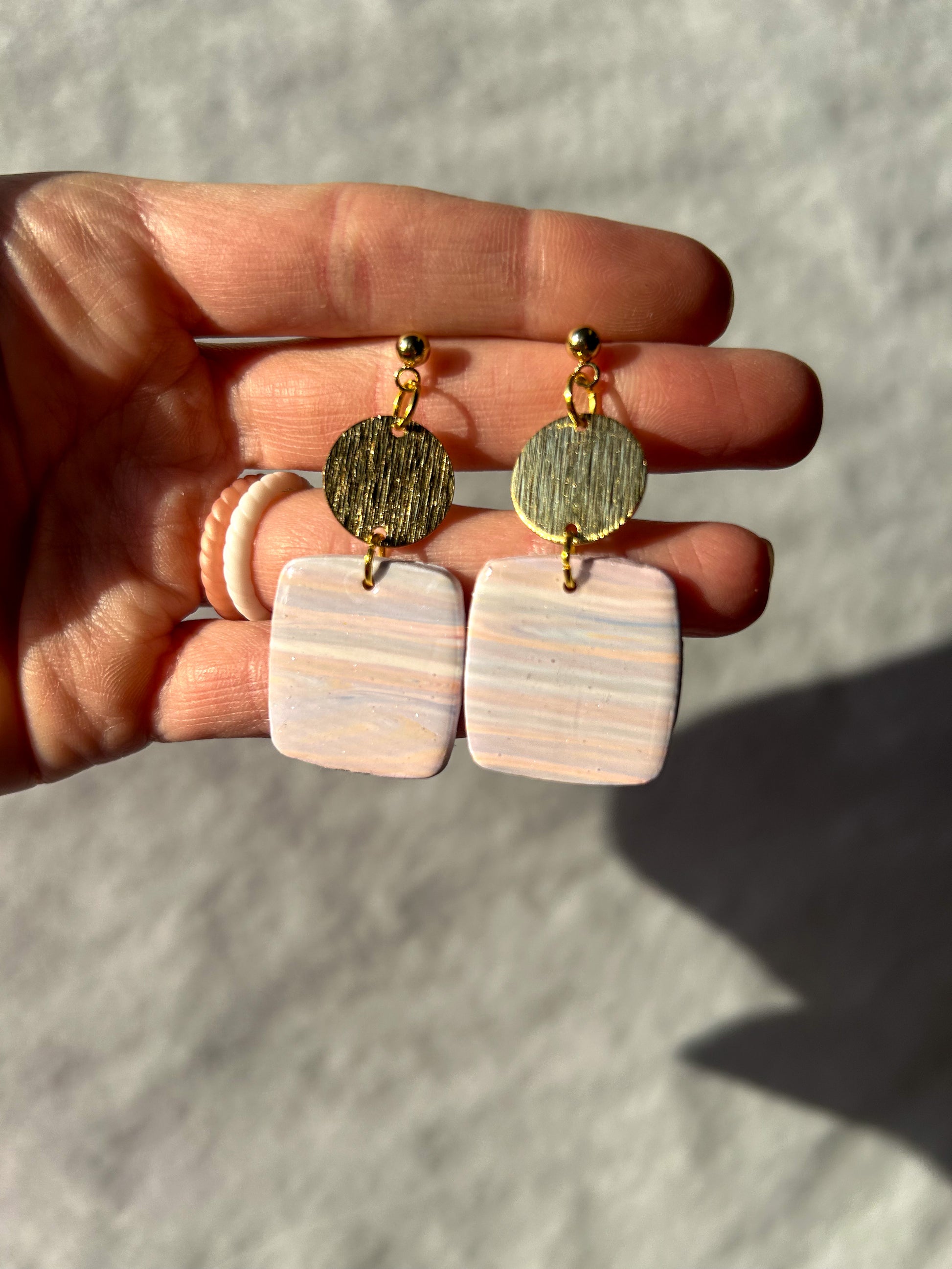 Hand holding a pair of marble earrings against a neutral background