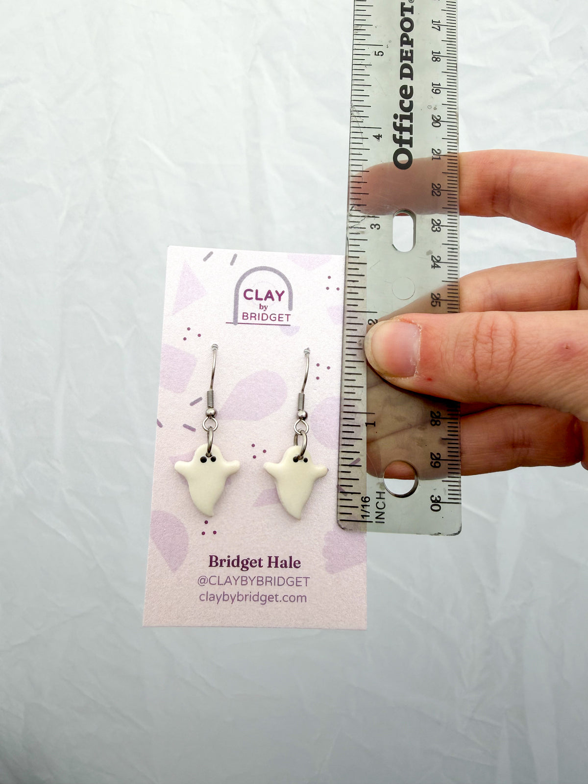 Hand holding a pair of earrings next to a ruler. Around 1.5 inches in length. 