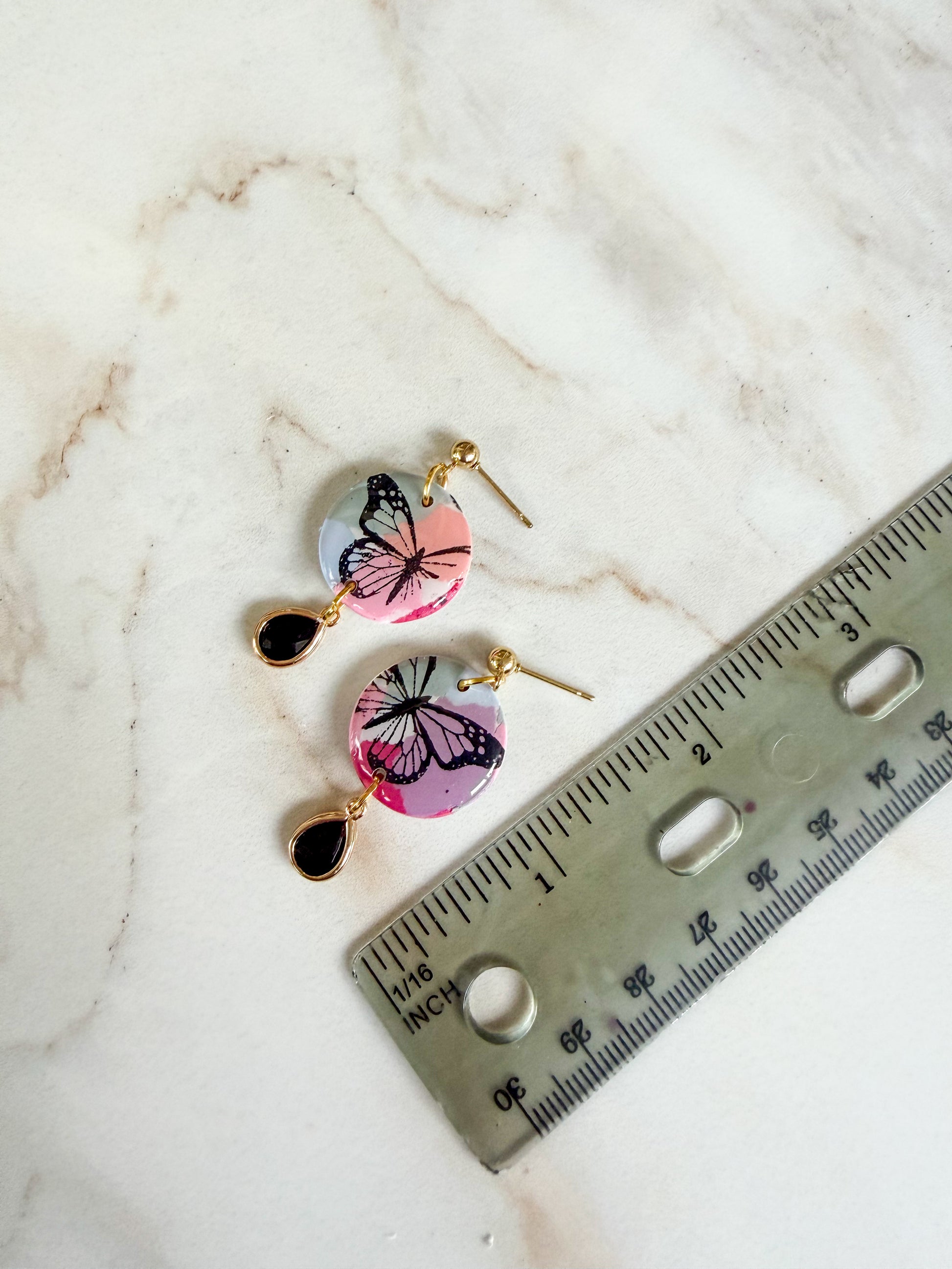 Butterfly-shaped earrings on a marble surface with a ruler for scale. About an inch and a half long. 