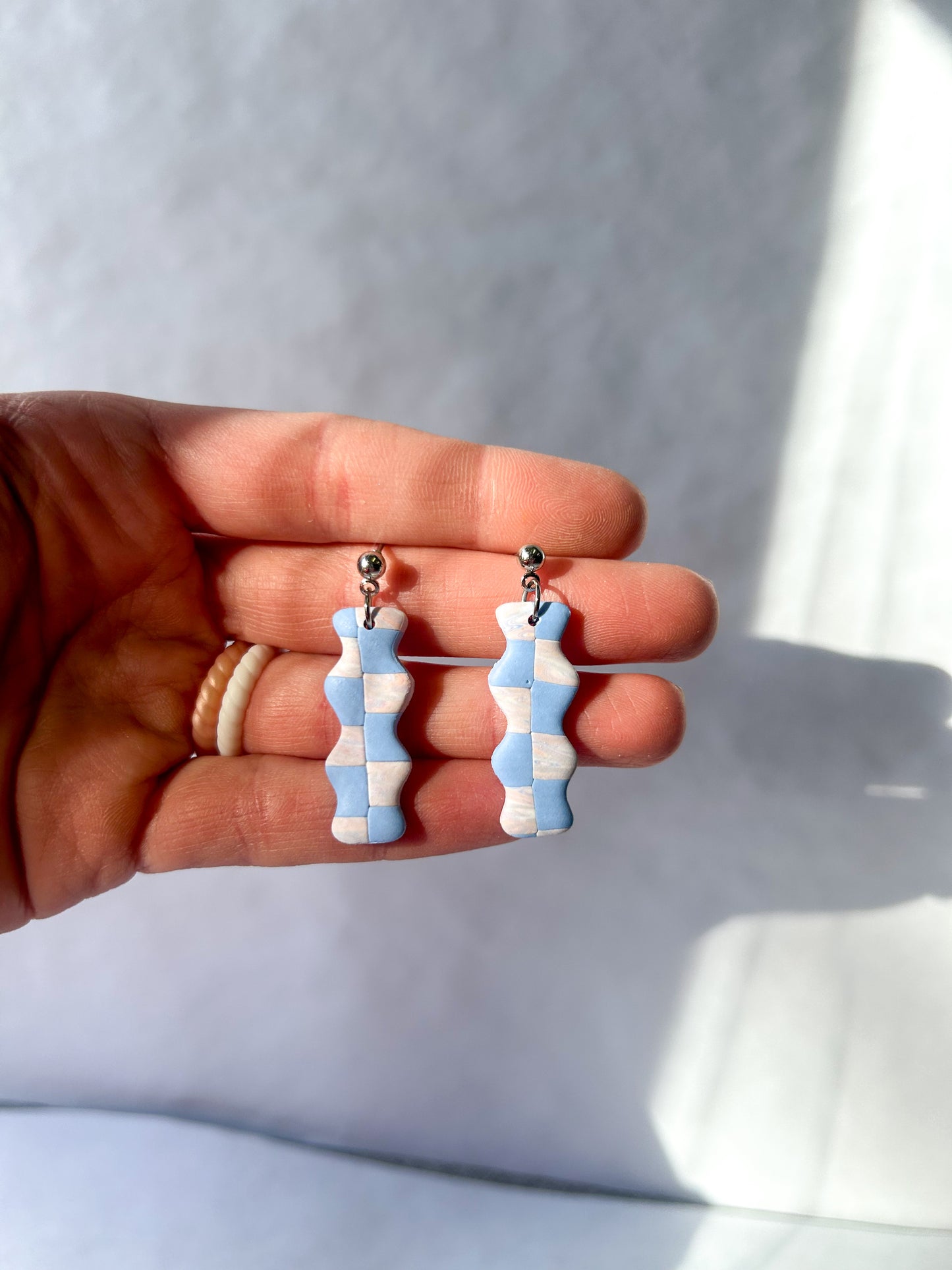 Checkered earrings held in a hand against a light background