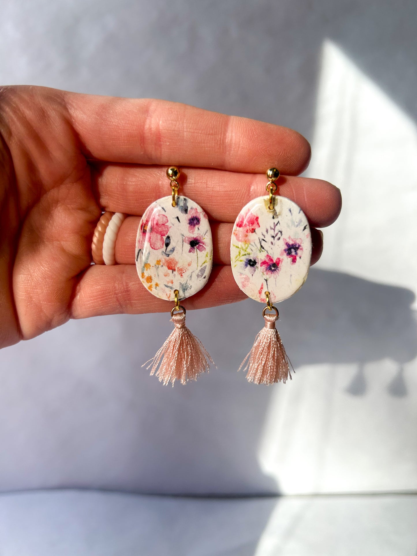 Hand holding floral earrings with tassels against a light background