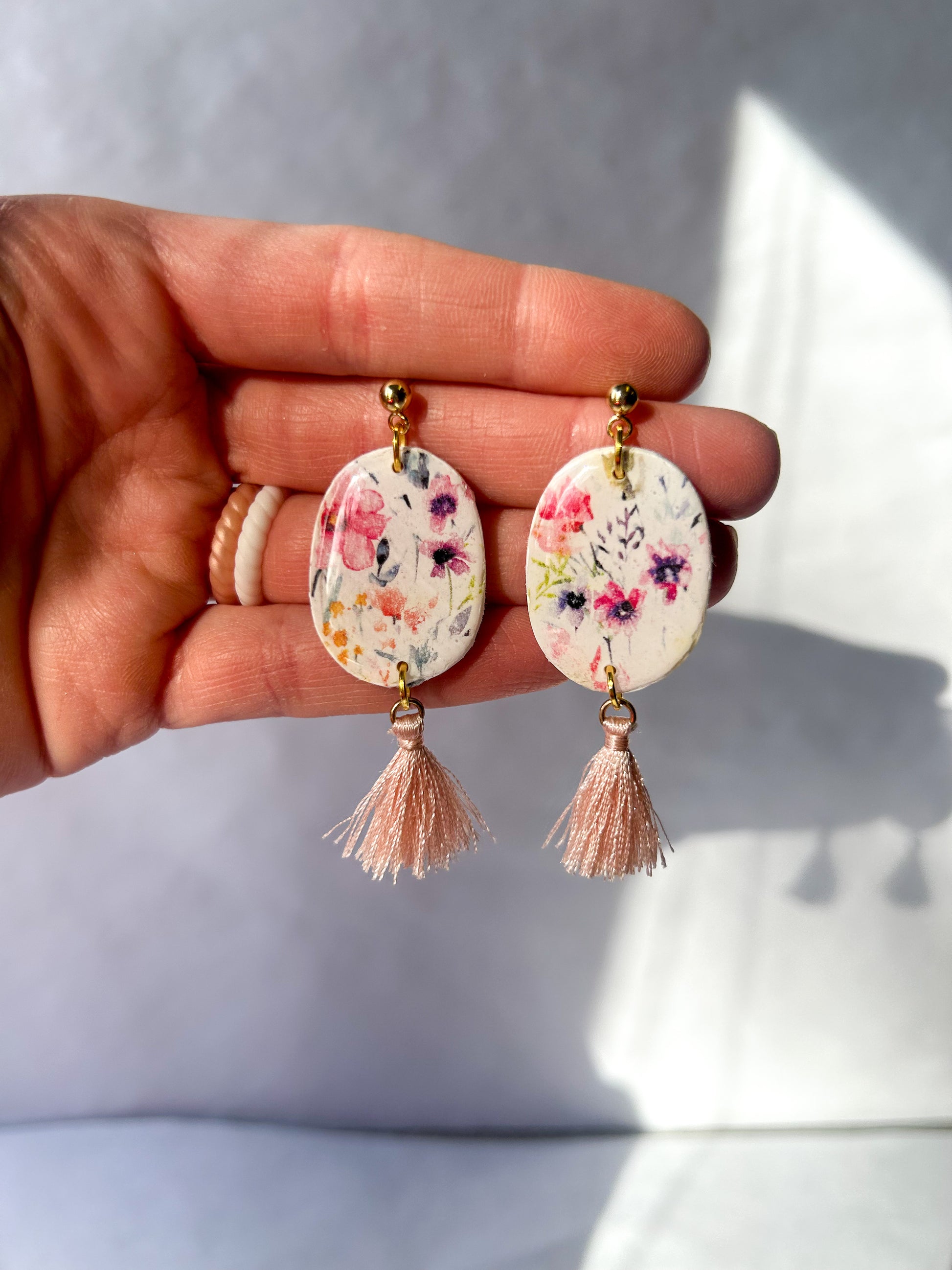 Hand holding floral earrings with tassels against a light background