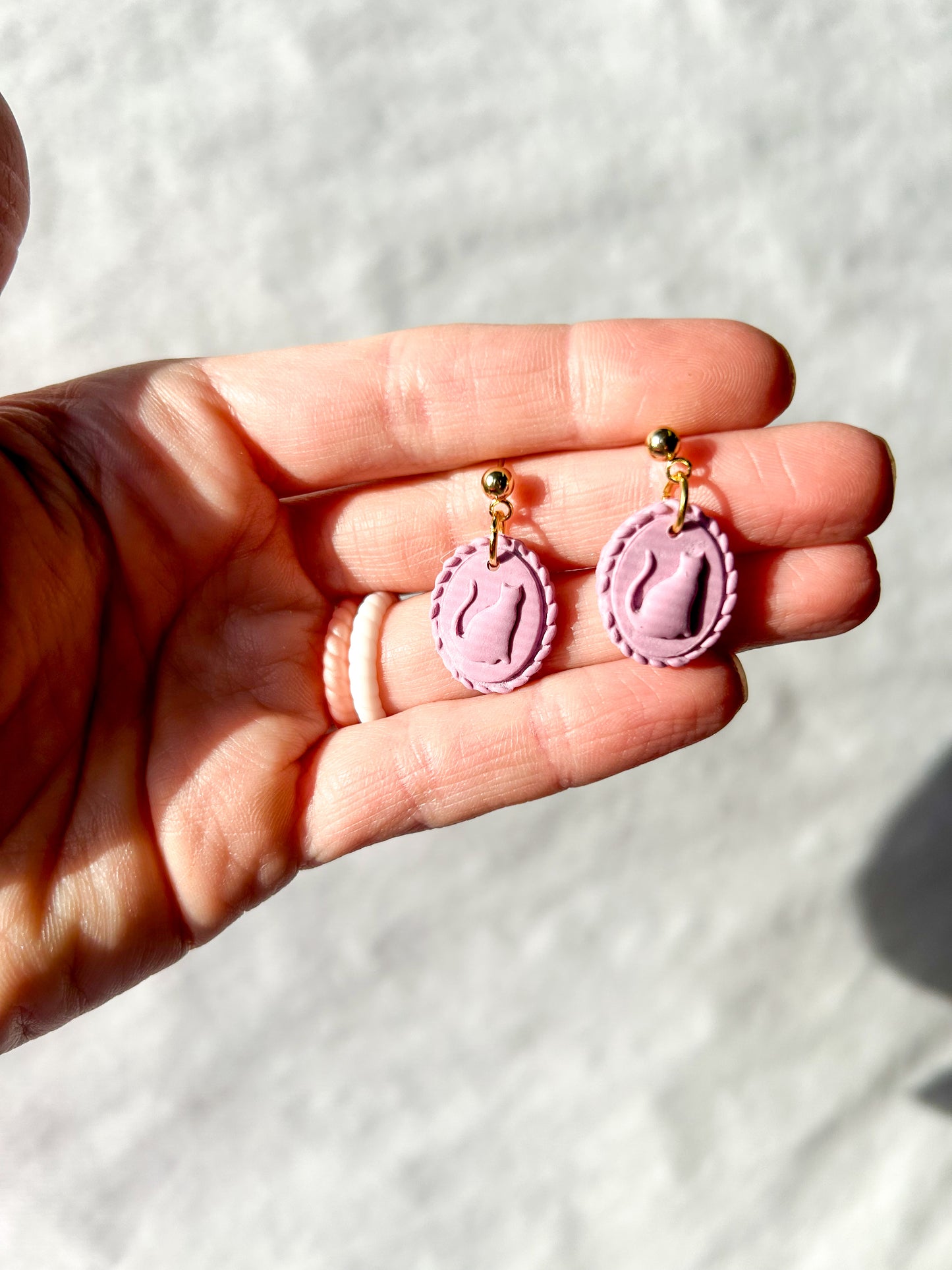 Purple earrings held in a hand against a light background