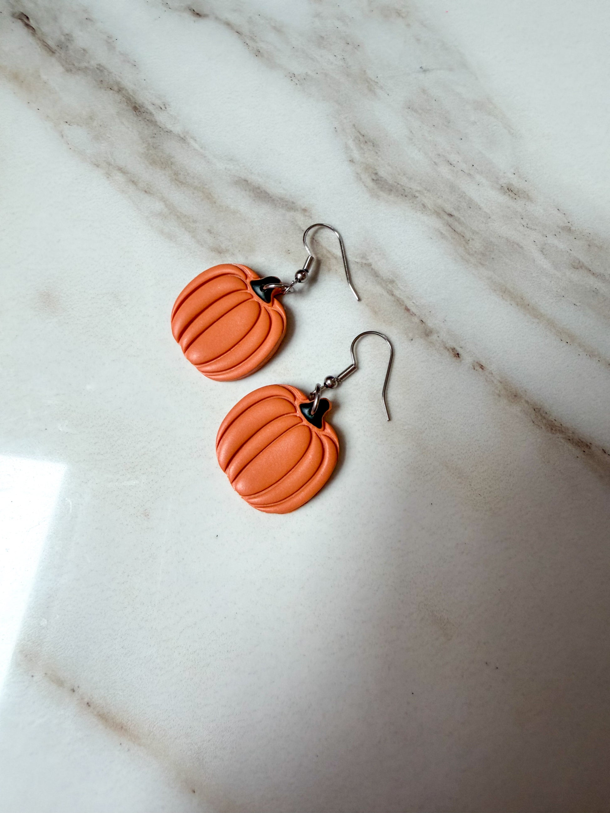 Pumpkin earrings with silver fishhooks on a marble surface 