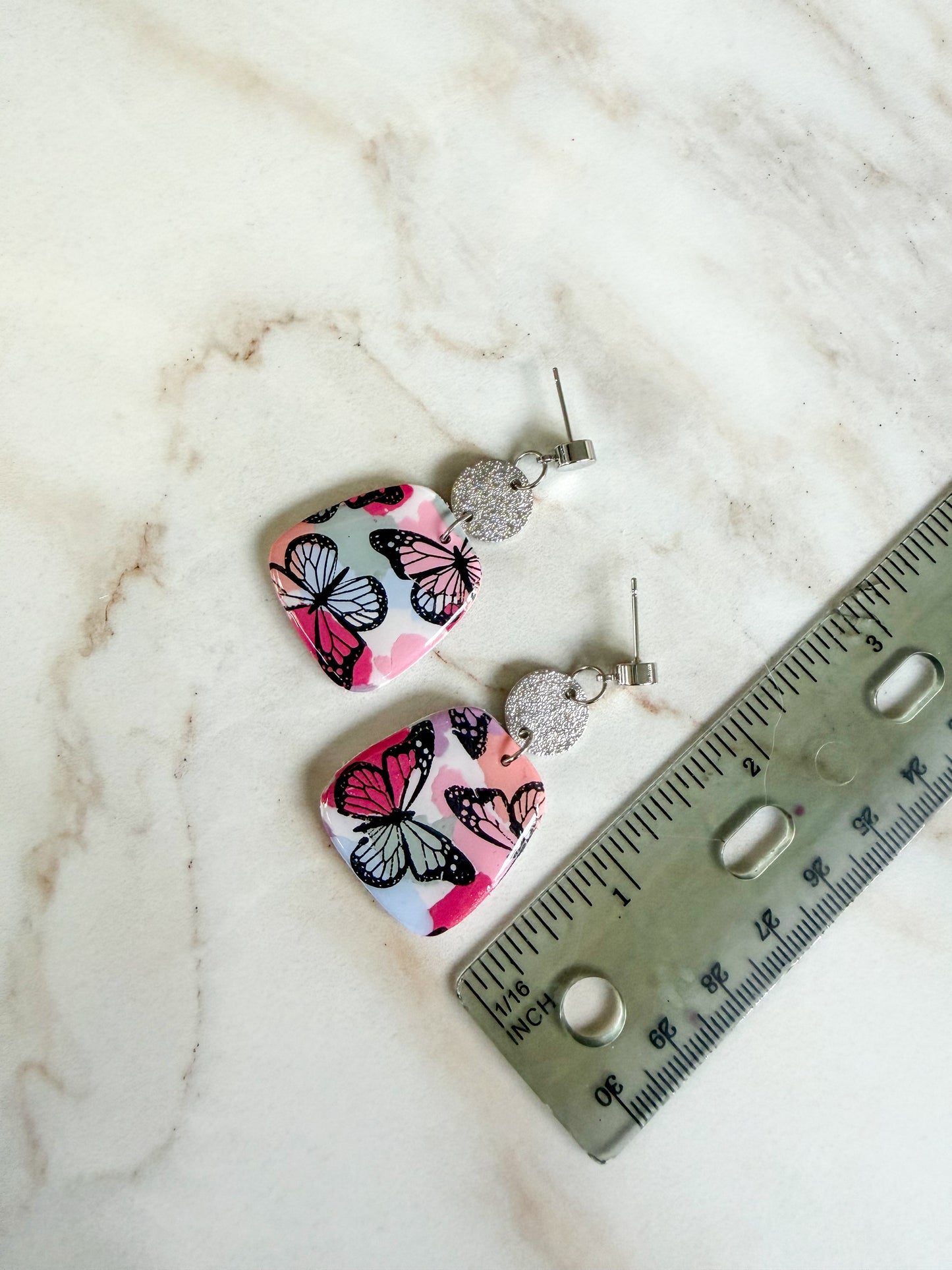 Butterfly-patterned earrings on a marble surface with a ruler for scale. About 2 inches long 