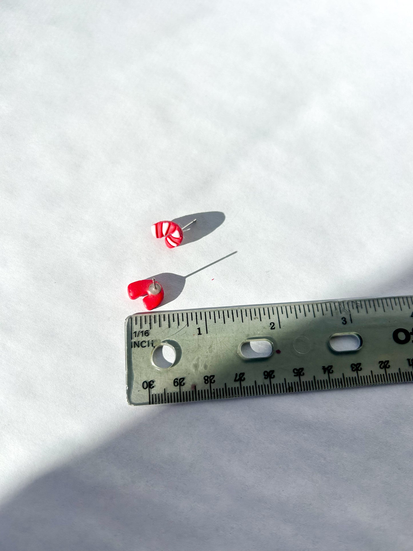 Small candy cane studs with a white background and a ruler for scale.