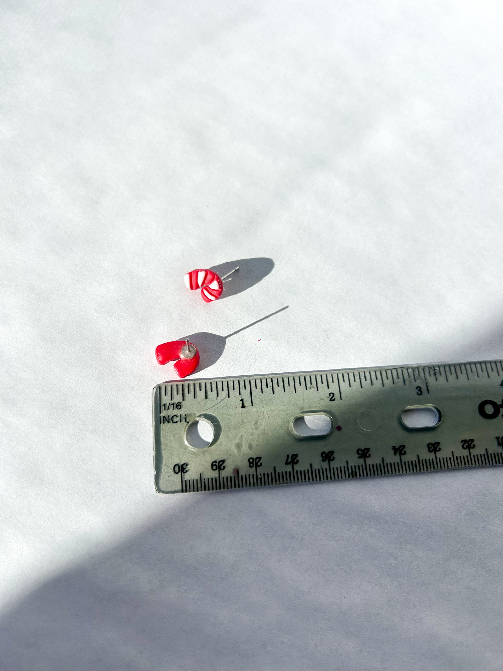 Small candy cane studs with a white background and a ruler for scale.