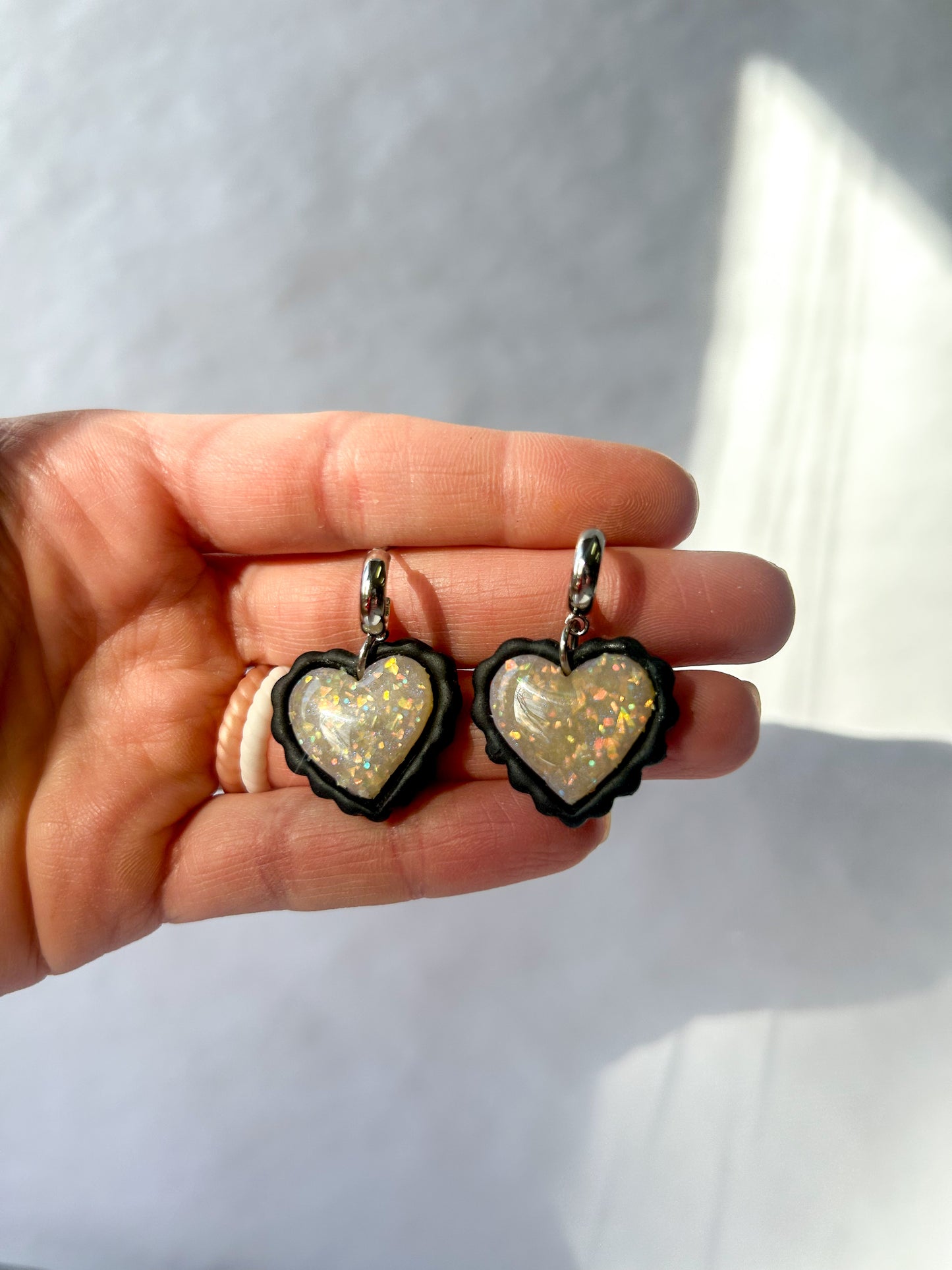 Heart-shaped earrings held in a hand against a light background. Black outside. Opalite inside 