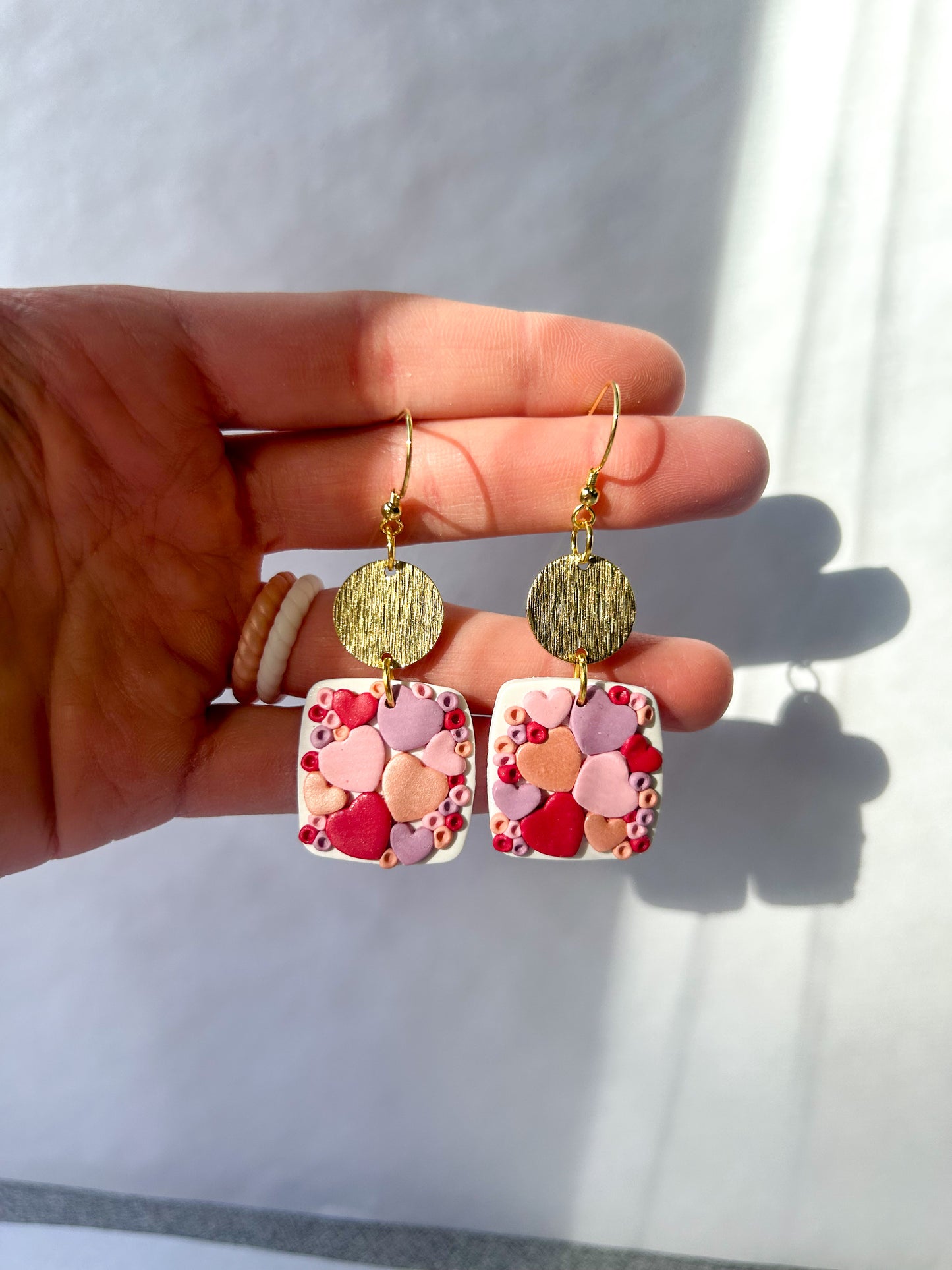 Hand holding a pair of earrings with heart patterns against a white background