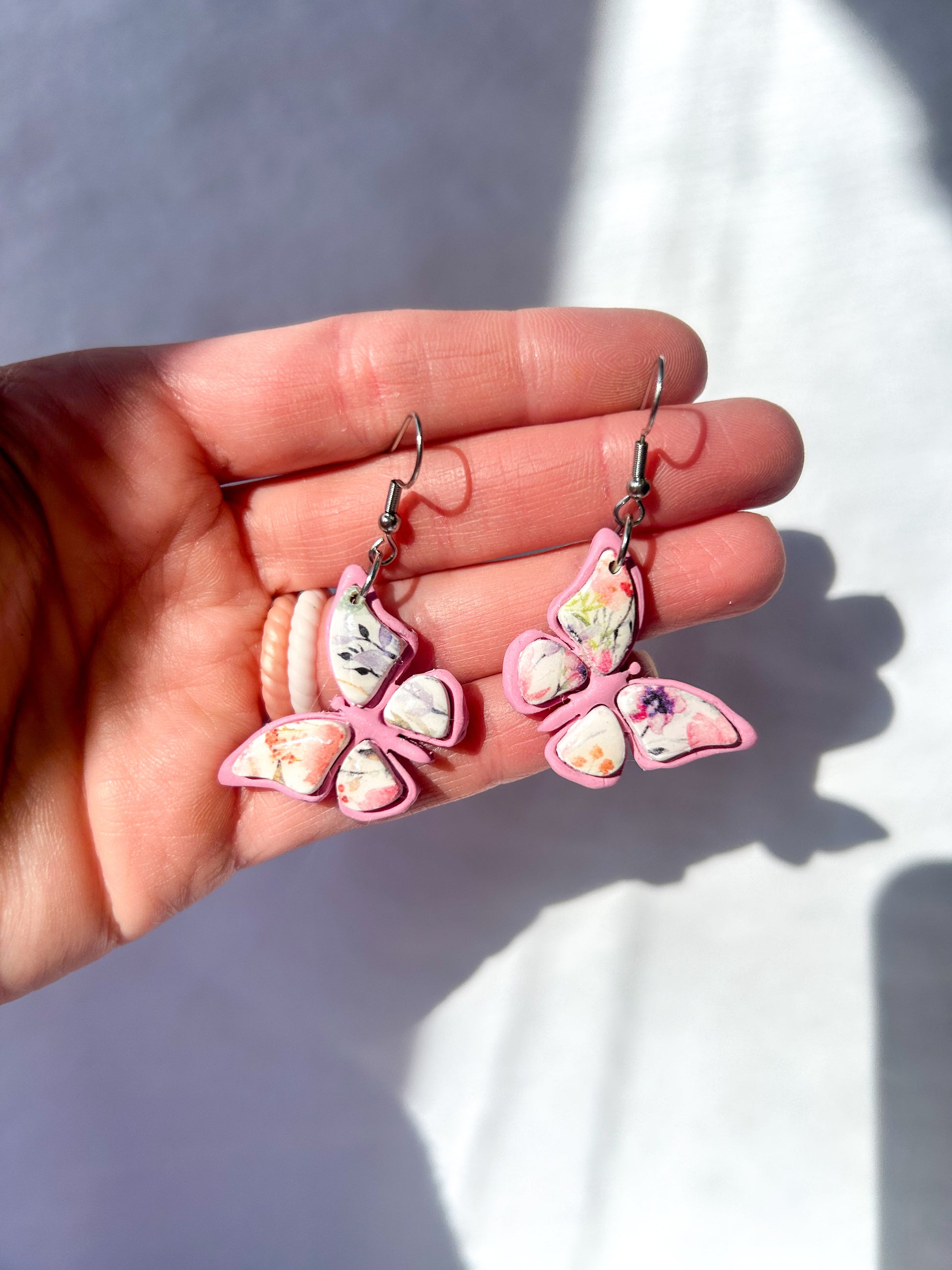 Pink butterfly earrings held in a hand with a blurred background