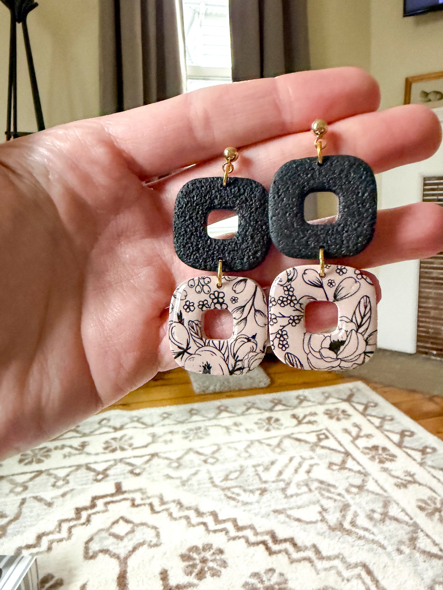 Hand holding a pair of earrings with black and patterned designs.