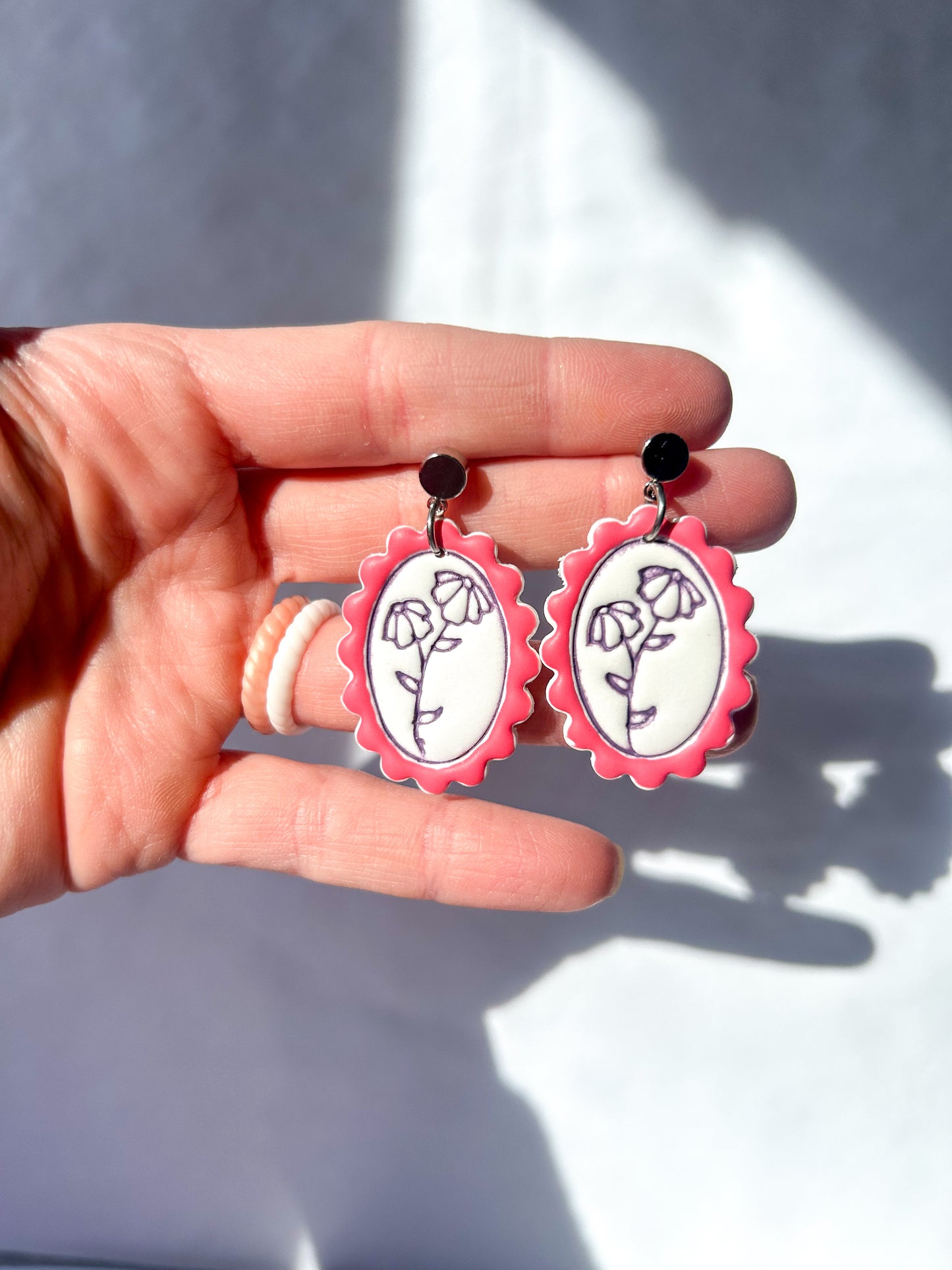 Hand holding pink earrings with floral designs against a neutral background