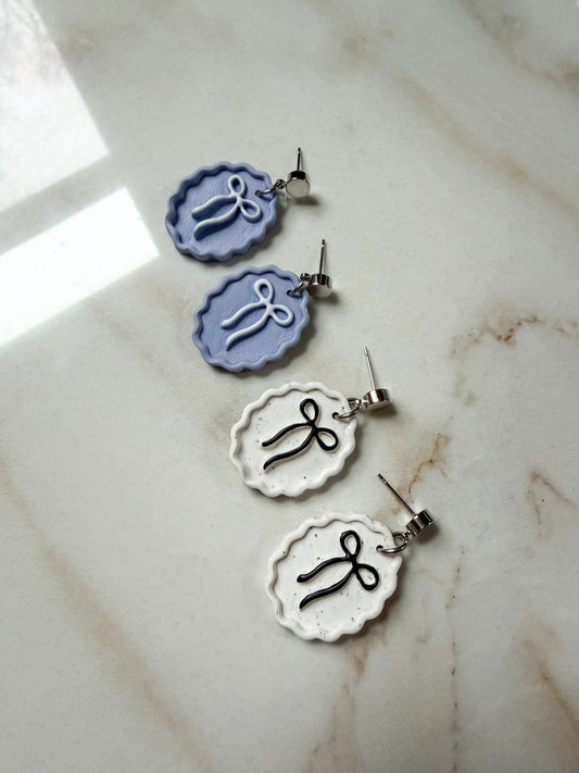 Two pairs of earrings with bows in the center laying on a marble surface.