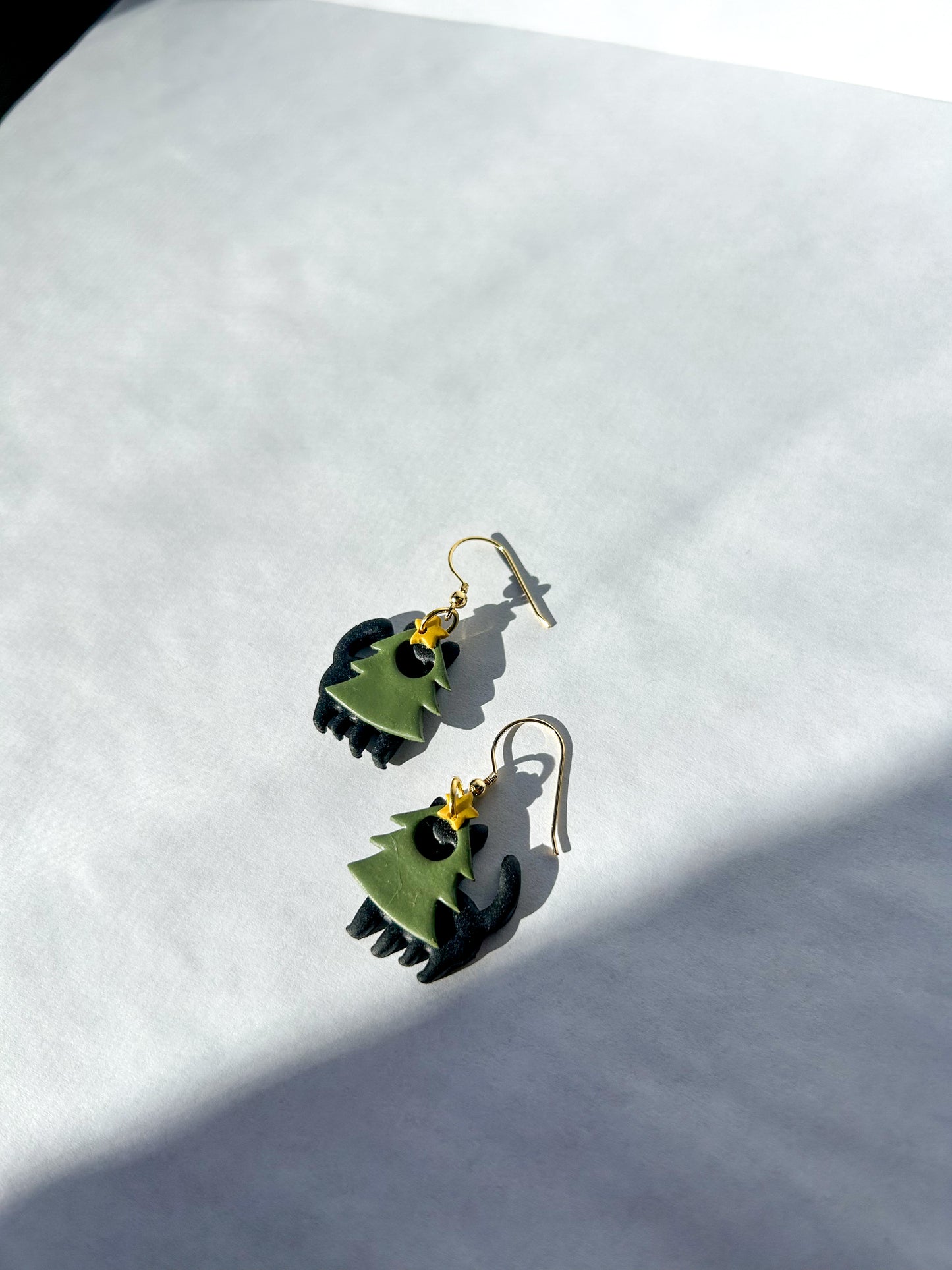 Pair of green and black earrings on a white surface. These are black cats wearing green tree costumes