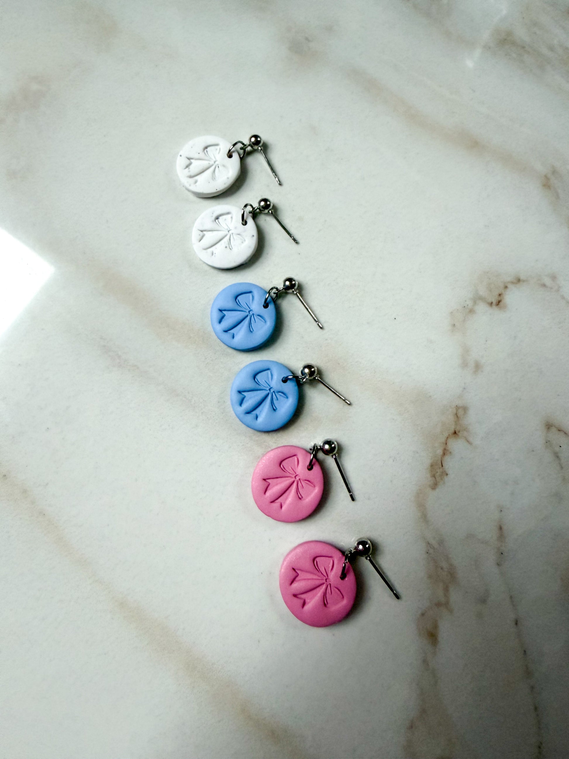 Three pairs of circle earrings with a bow shaped stamp in the middle