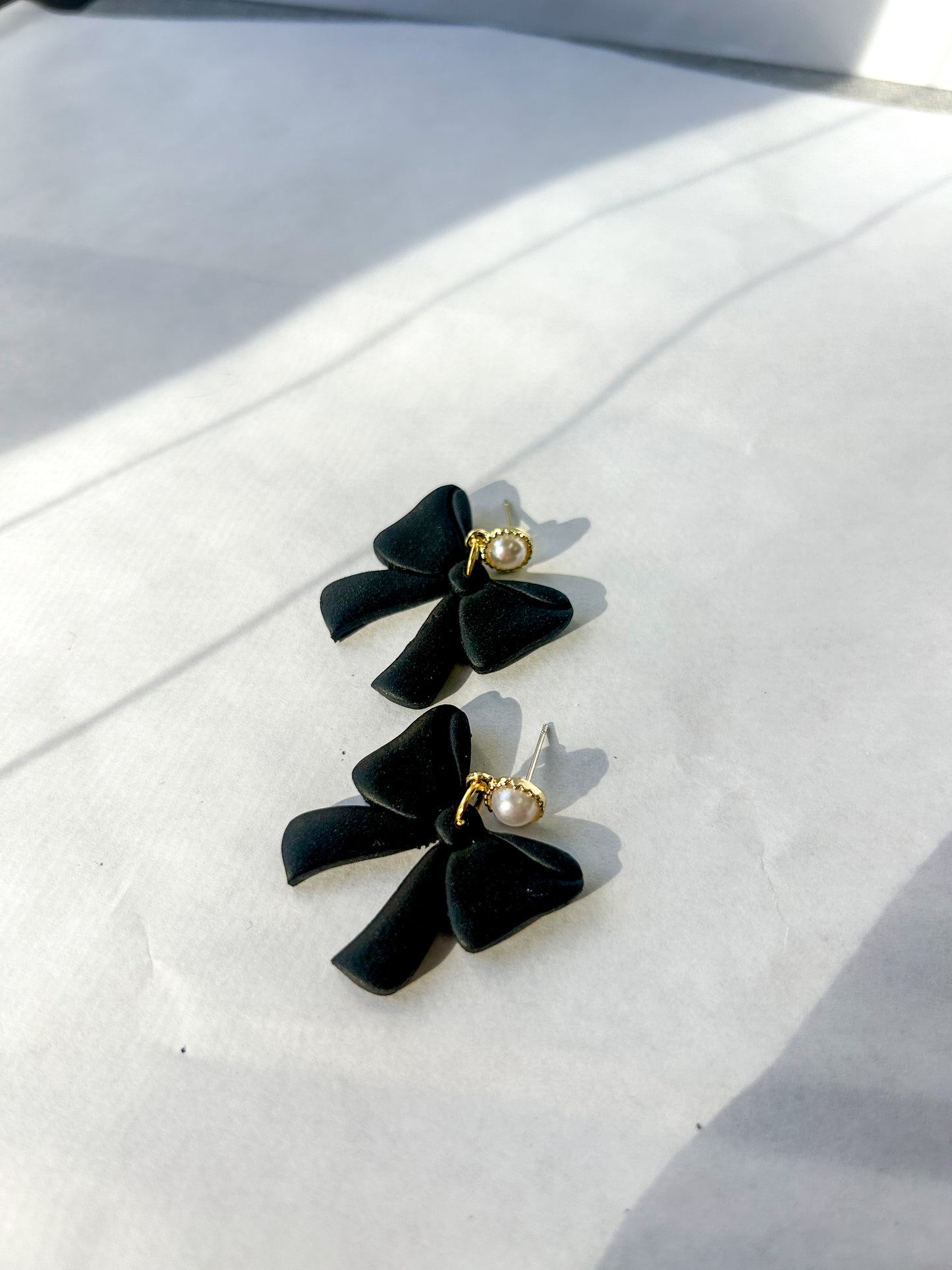 Black bow-shaped earrings with pearl center on a white surface