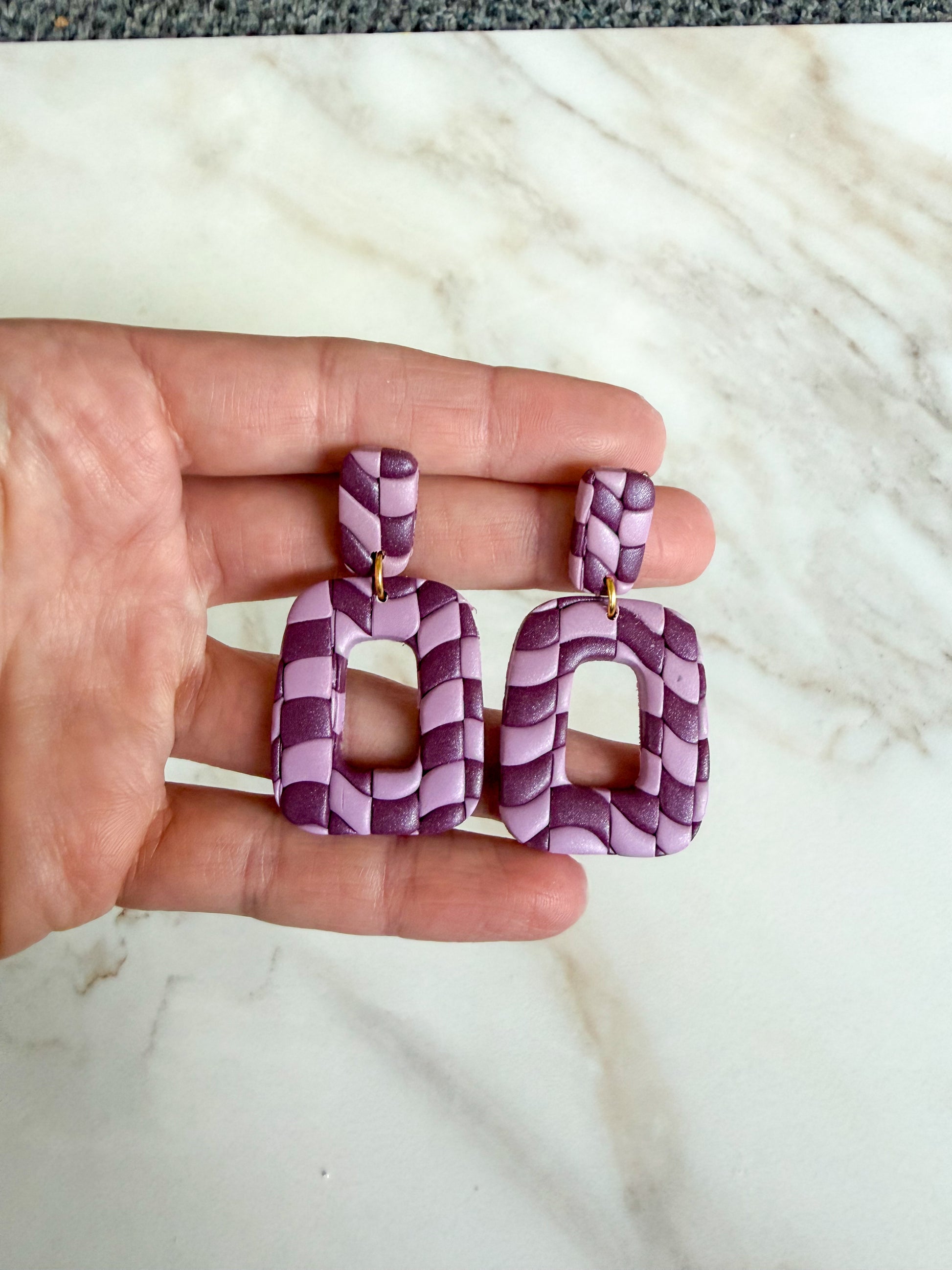 Purple woven earrings held in a hand against a marble background