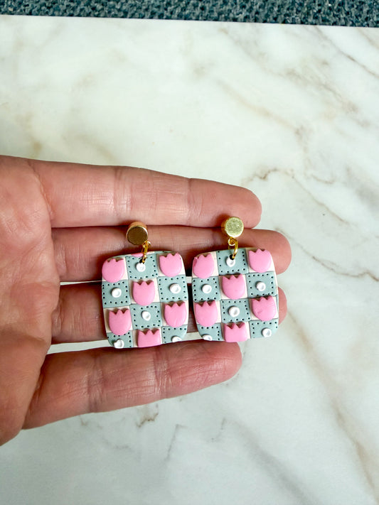 Checkered earrings with pink and white pattern held between fingers on a marble background