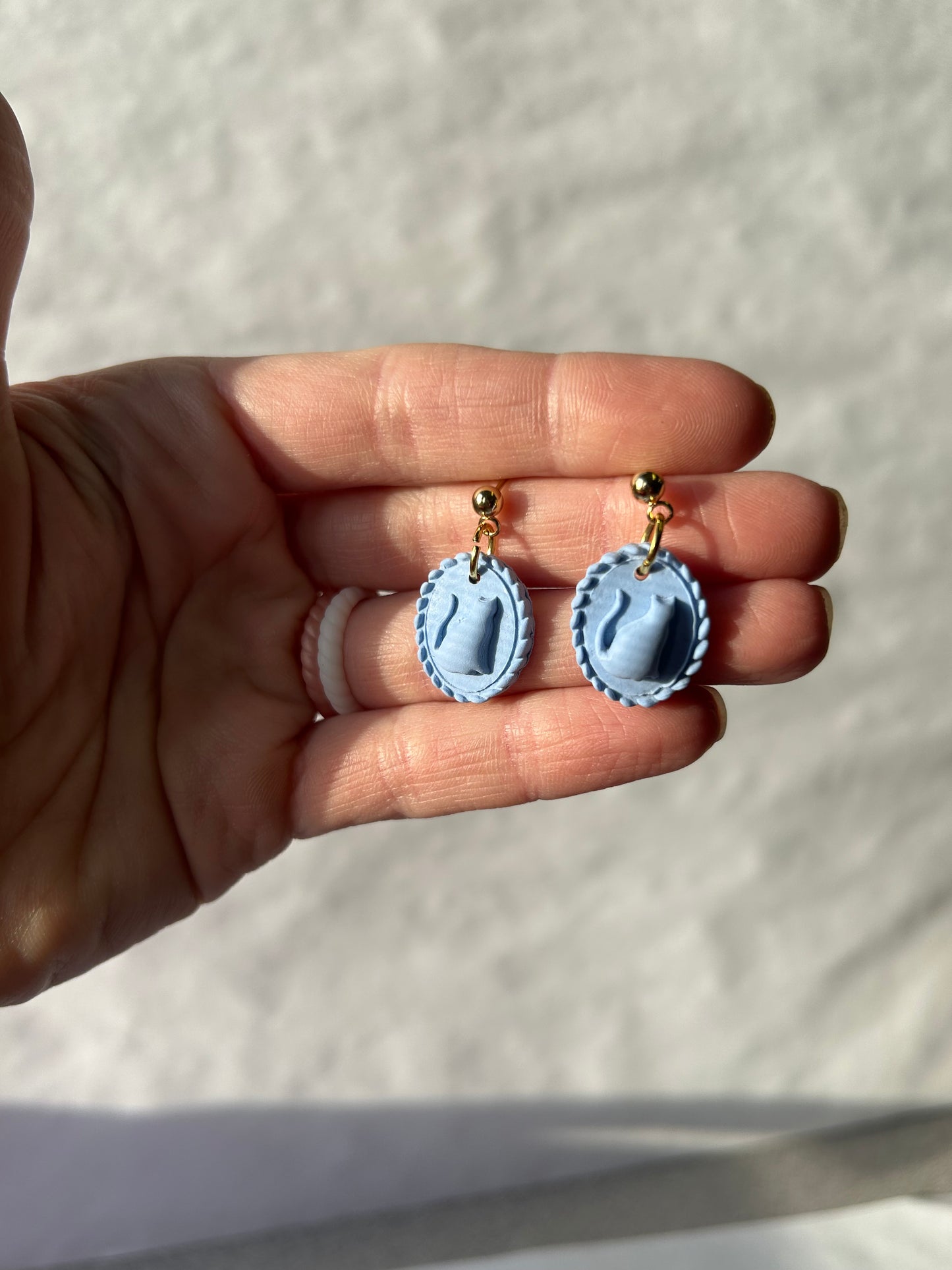 Hand holding a pair of small blue and gold earrings against a neutral background