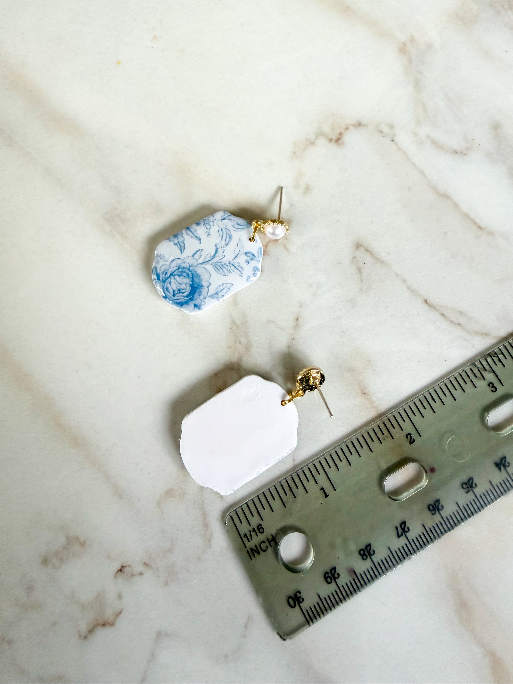 Two earrings on a marble surface with a ruler for scale. About an inch and a half long. 