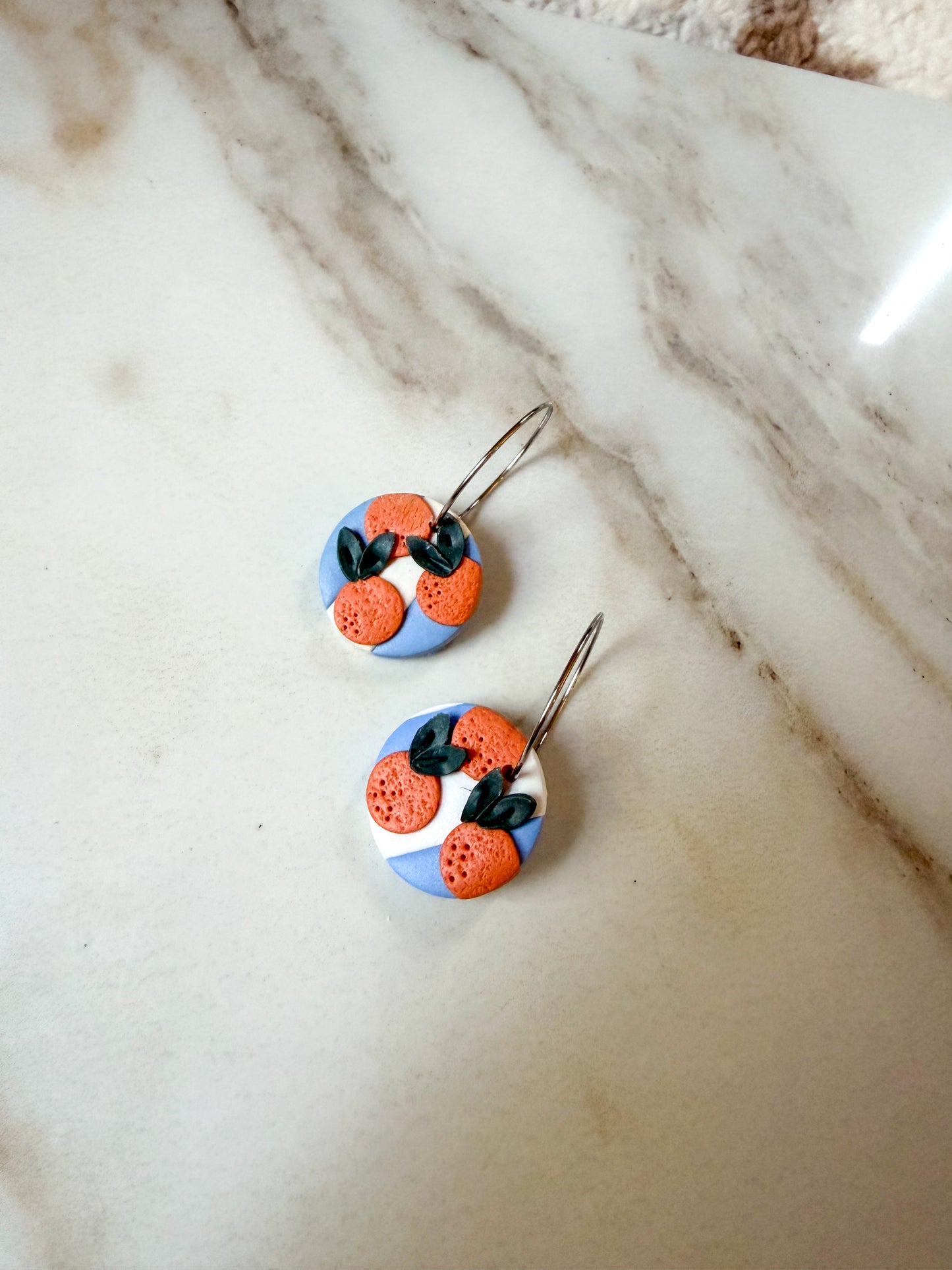 A pair of blue and white circle dangles with oranges on top. Hypoallergenic stainless steel hoops. 